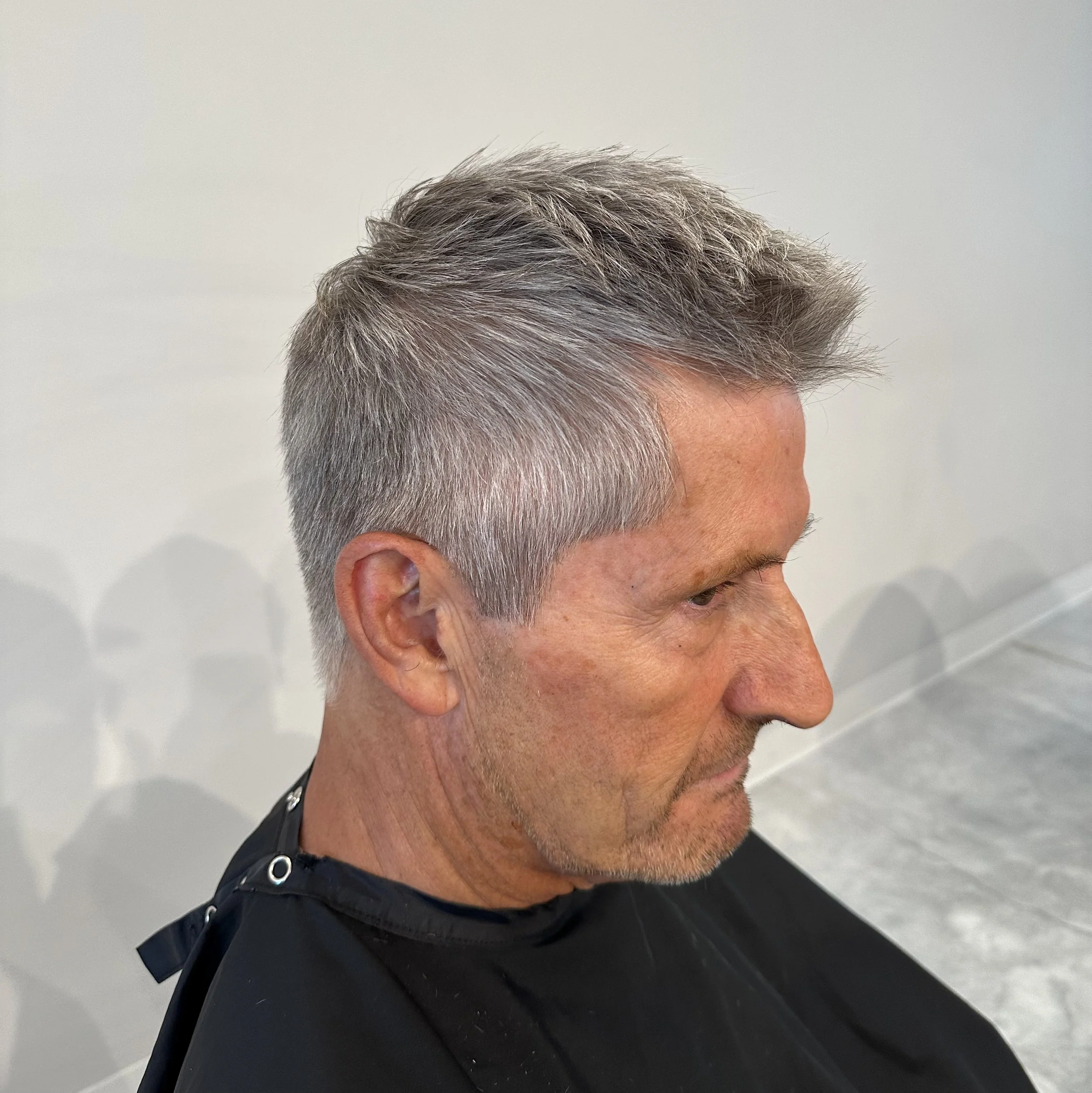 Side view of a middle-aged man with short, gray hair at a hair salon.