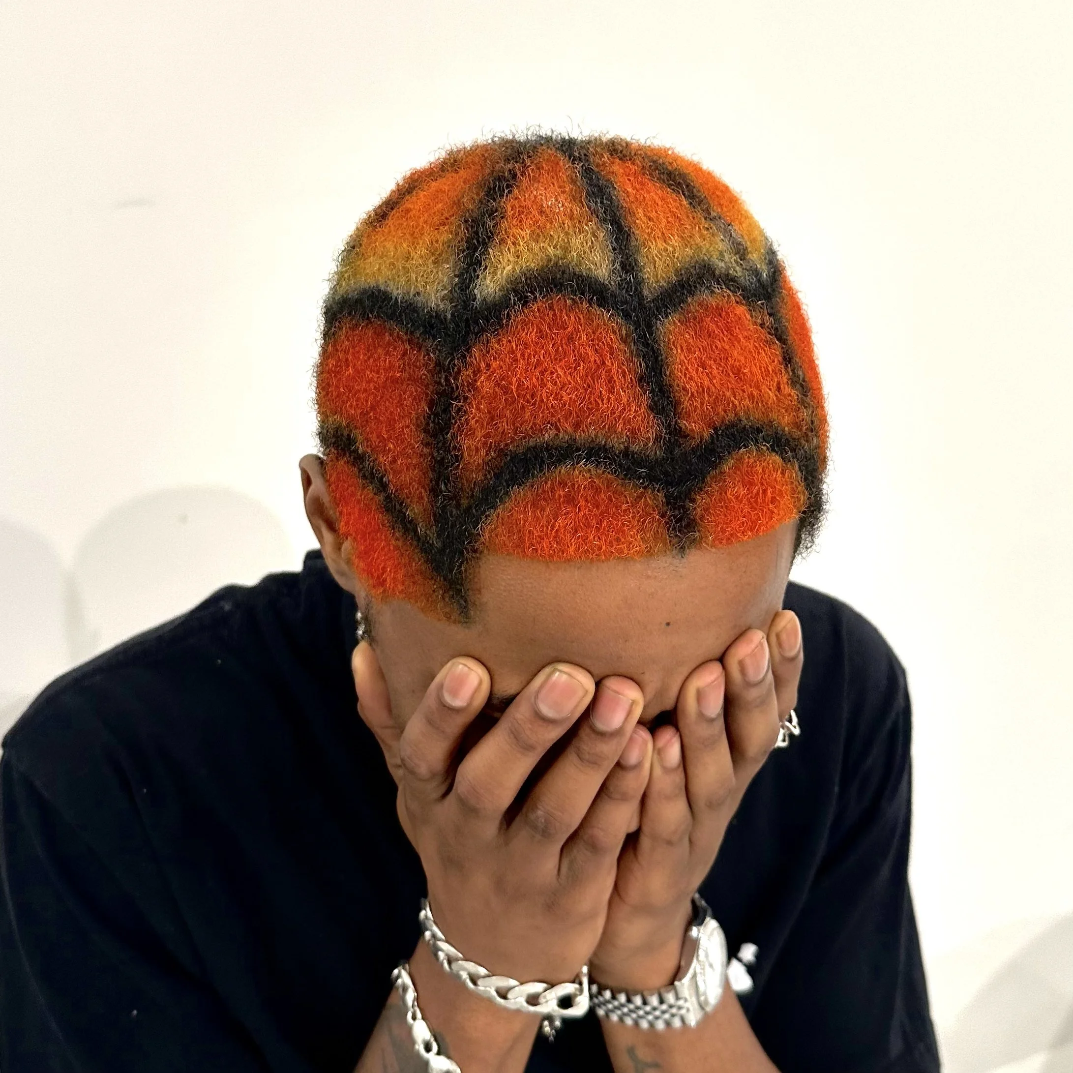 Person with short hair covered in colorful, Spider-Man themed hair dye, covering their face with hands.