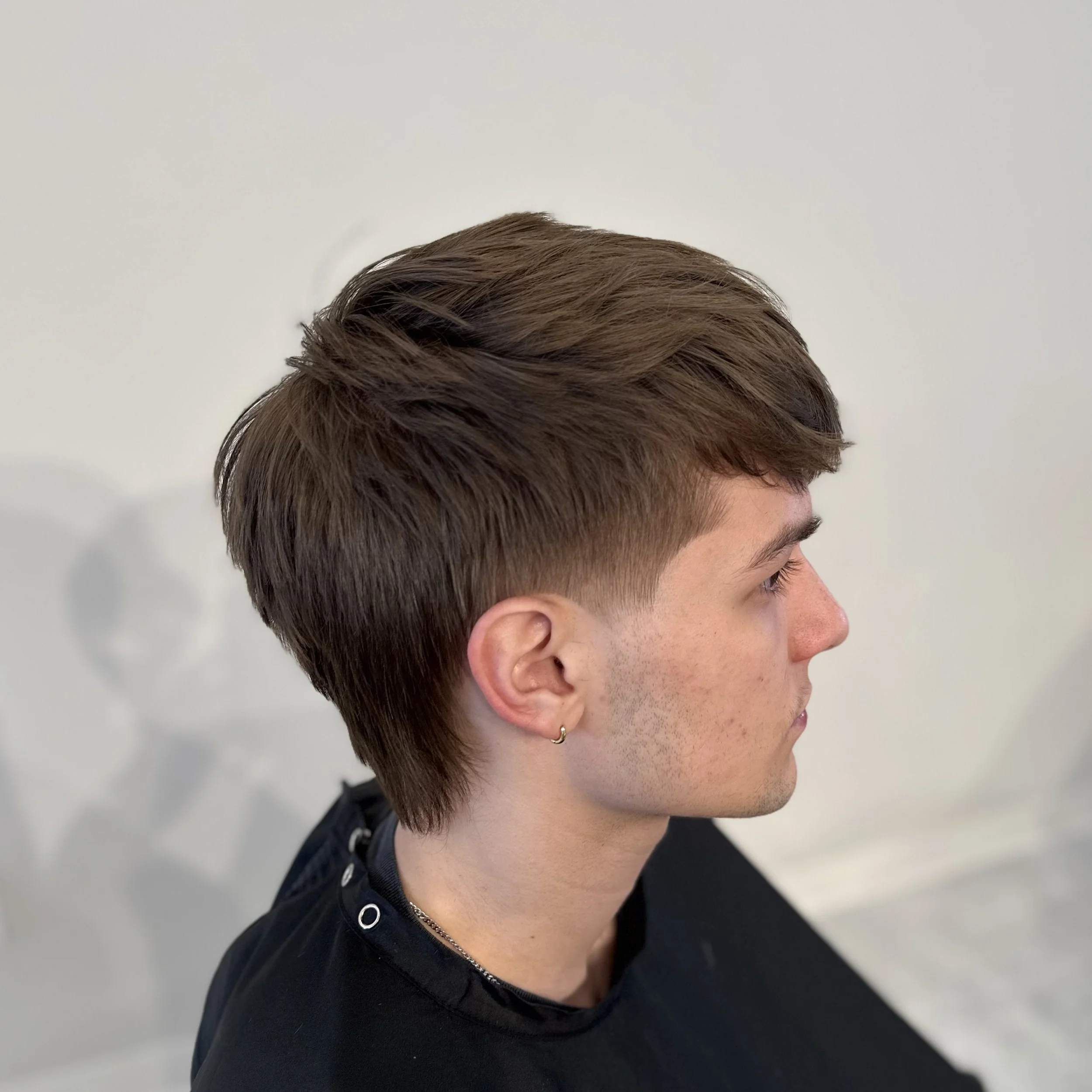 Side profile of a young man with a short layered haircut and a small earring.
