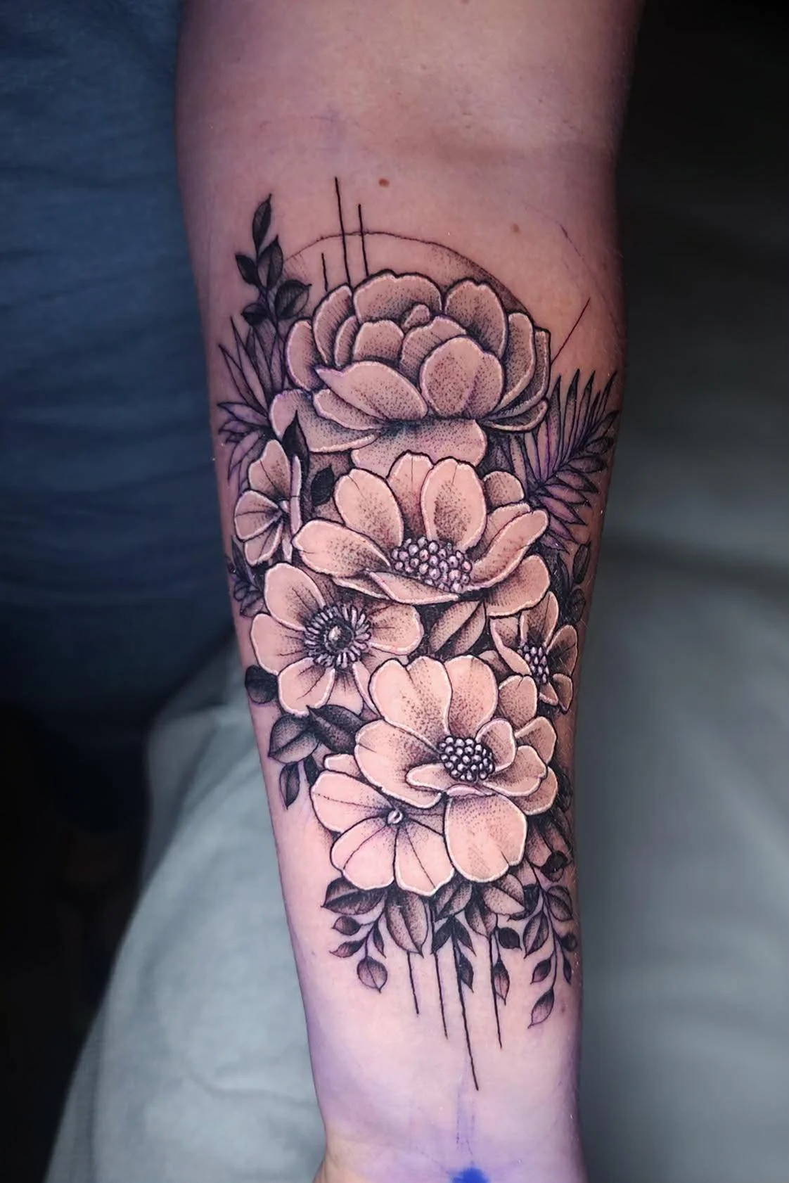 Black and white floral tattoo on forearm featuring large roses, smaller flowers, and leaves.