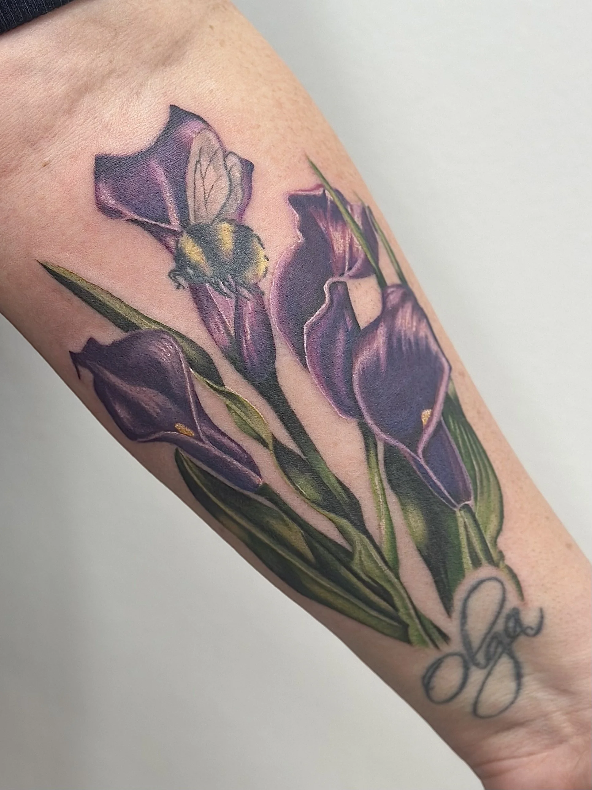 A colorful tattoo of purple irises and a bee on a person's arm.