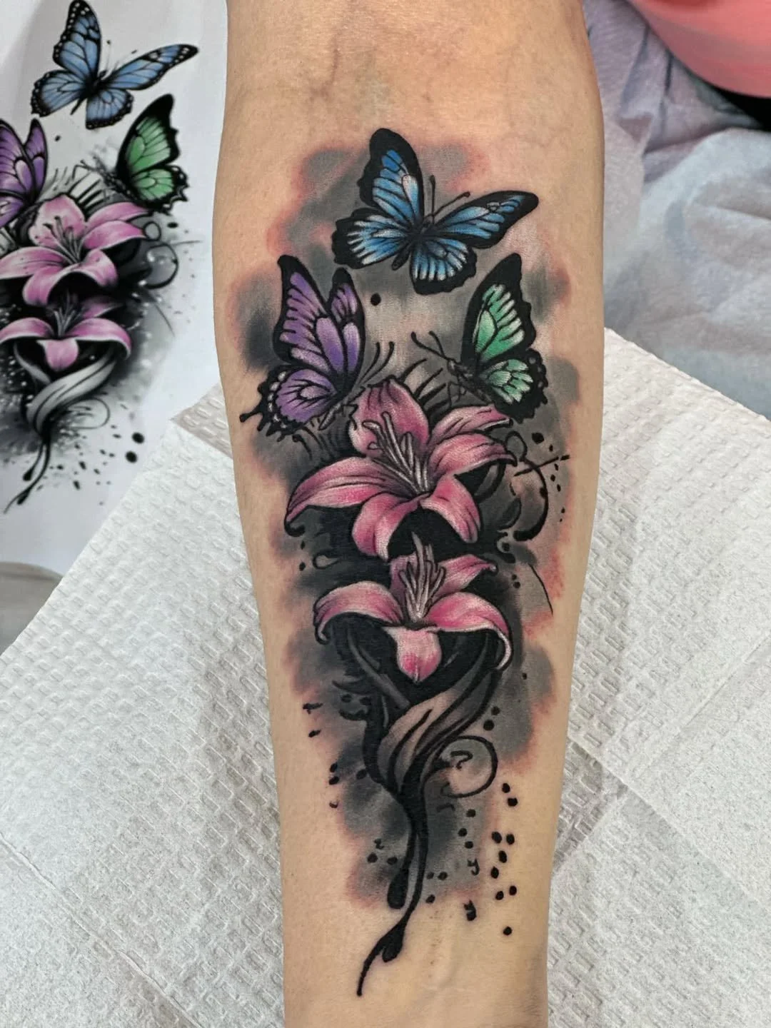 Colorful tattoo of pink lilies and blue, green, and purple butterflies on a person's arm.