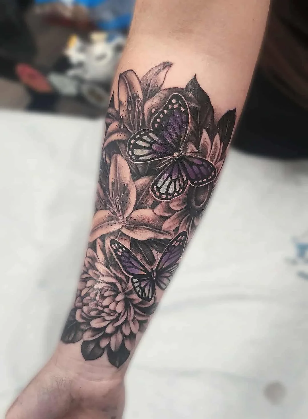 Black and gray tattoo of butterflies and flowers on a person's arm.