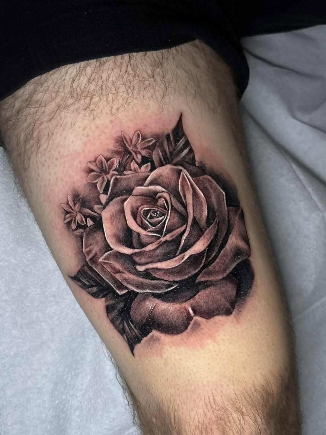 Black and gray tattoo of a realistic rose with smaller flowers surrounding it on a person's thigh.