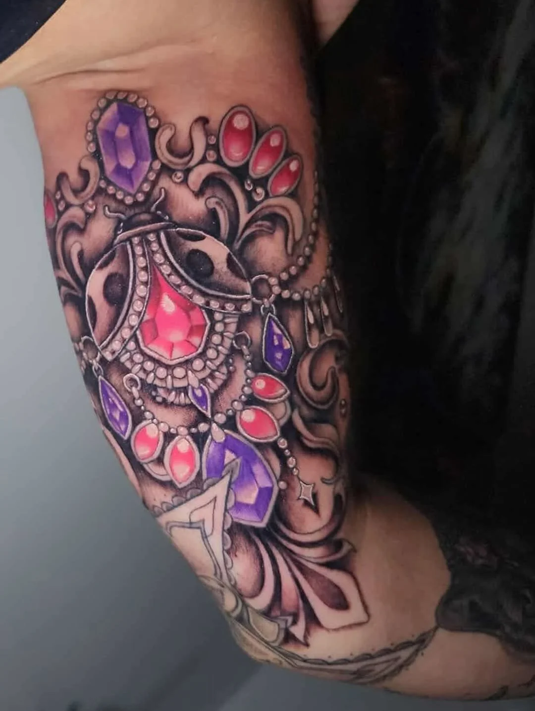 Colorful tattoo featuring jewelry and gemstone designs on a person's arm.