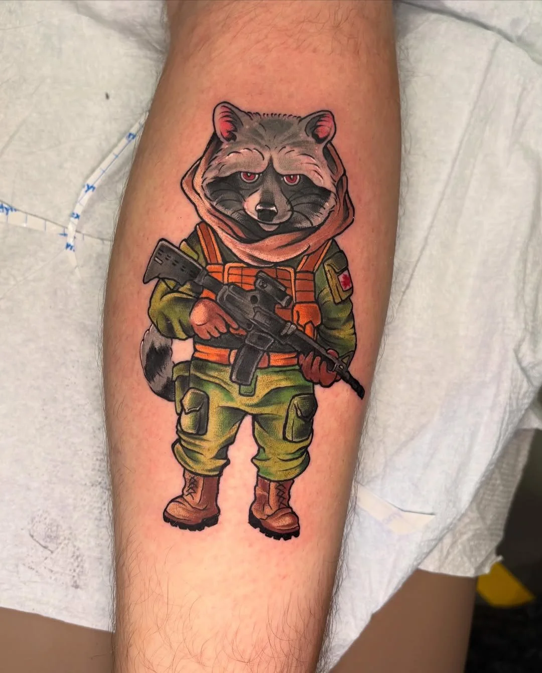 A tattoo of a raccoon dressed in military gear, holding a rifle, with a determined expression.
