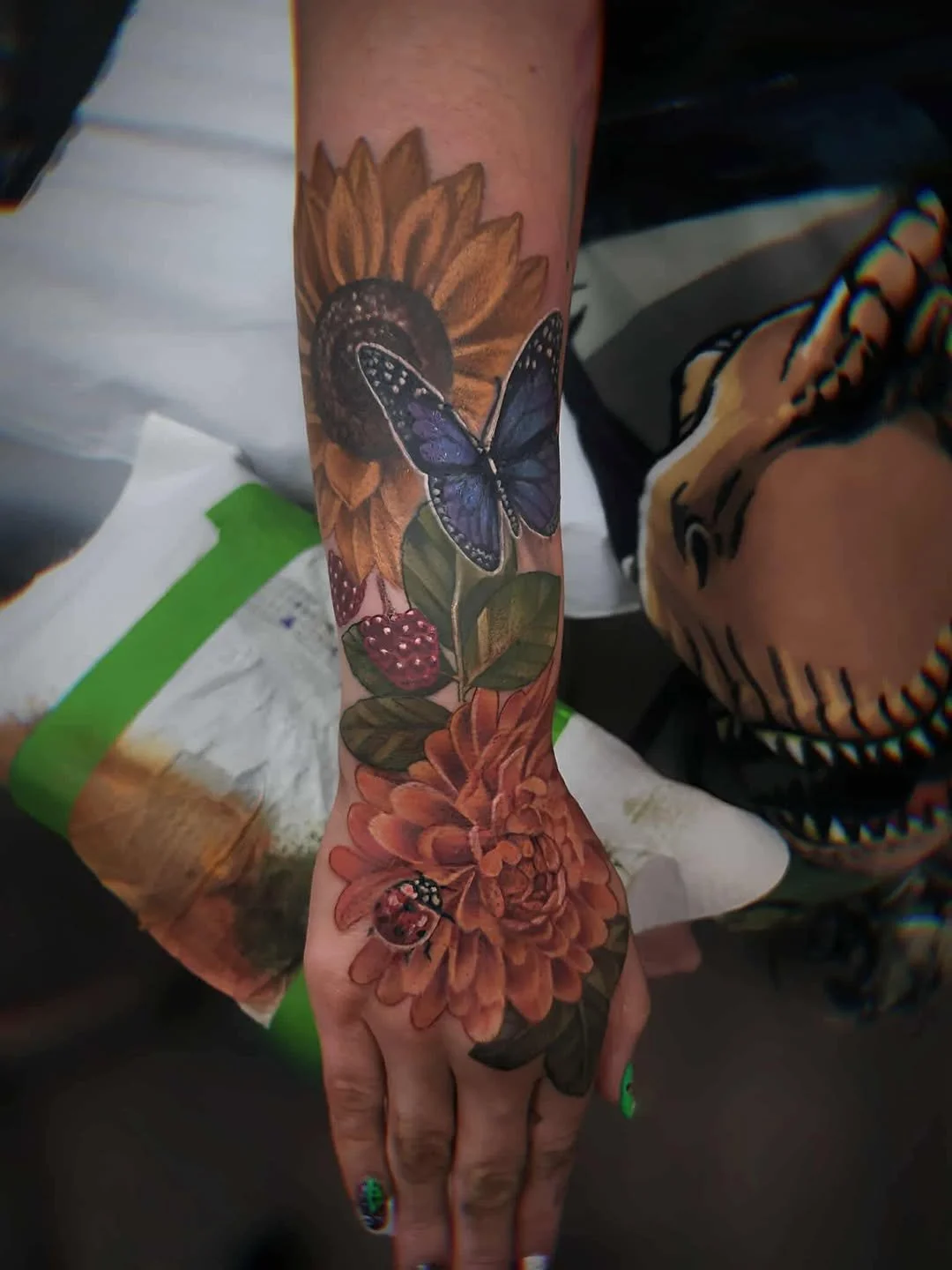 Tattoo of a sunflower, butterfly, berries, and flowers on a person's arm.