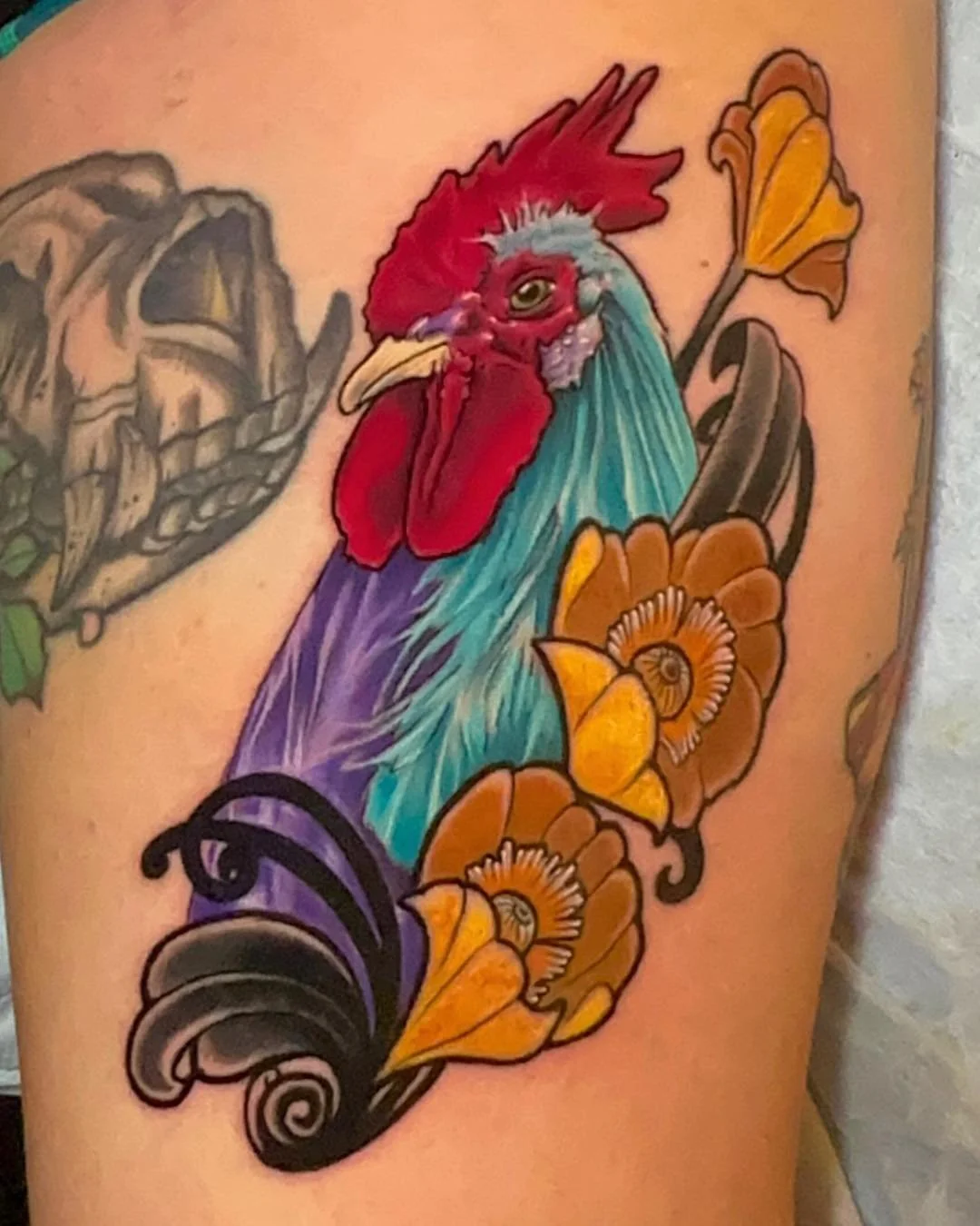Colorful tattoo of a rooster surrounded by orange flowers with black swirling accents.