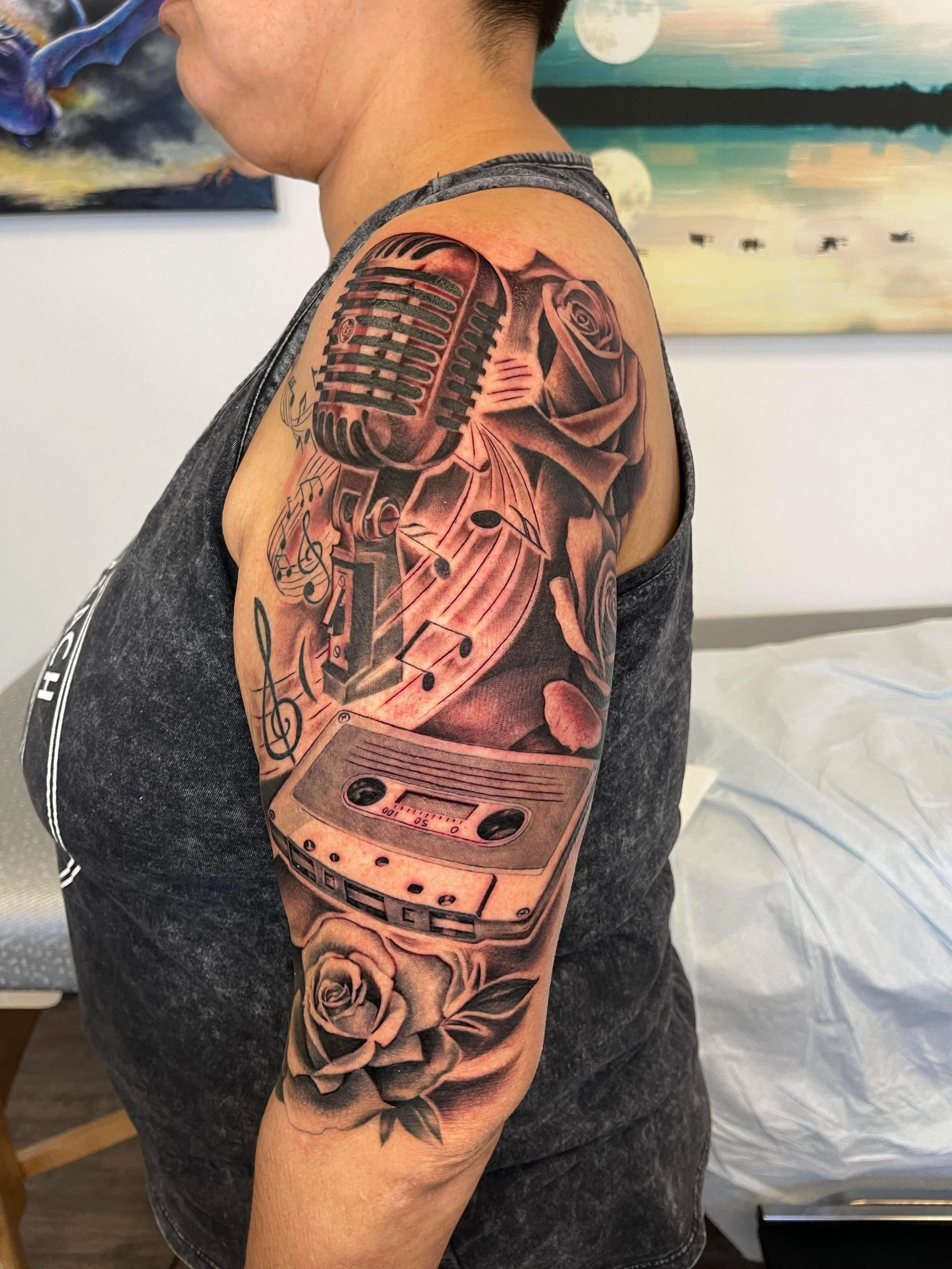 Tattoo of a vintage microphone, a cassette tape player, and roses on person's upper arm.
