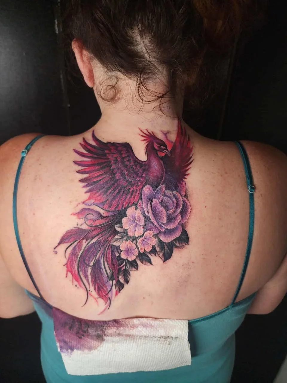 Colorful back tattoo featuring a phoenix with outstretched wings and flowers, including peonies and hydrangeas.
