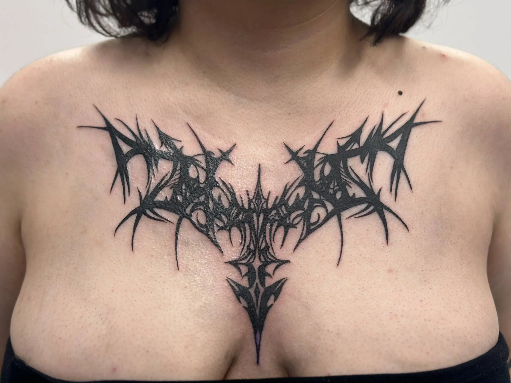 Black tribal-style tattoo on person's chest, featuring sharp, jagged lines resembling a symmetrical abstract design.
