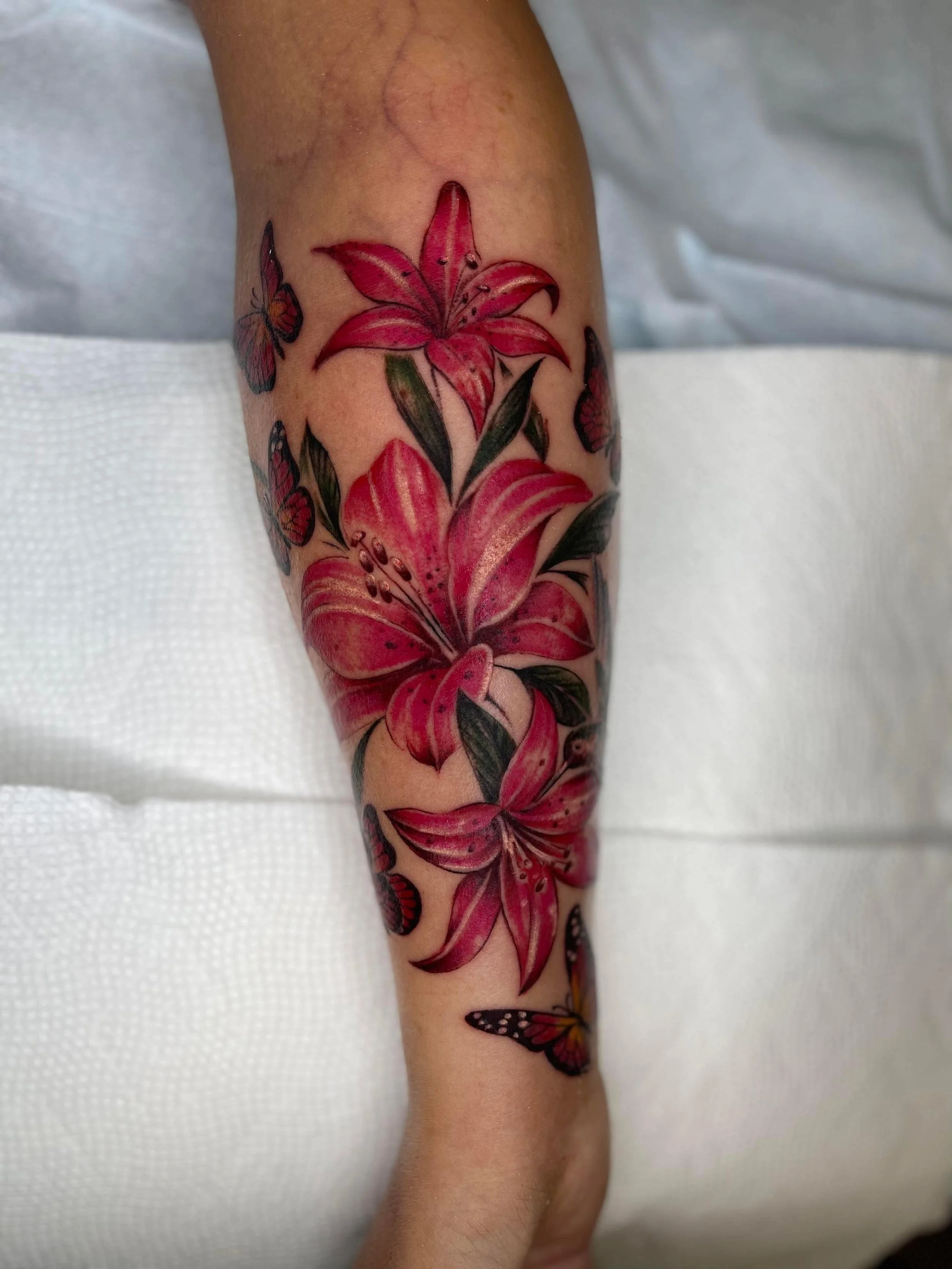 A colorful tattoo of pink lilies and butterflies on a person's forearm.