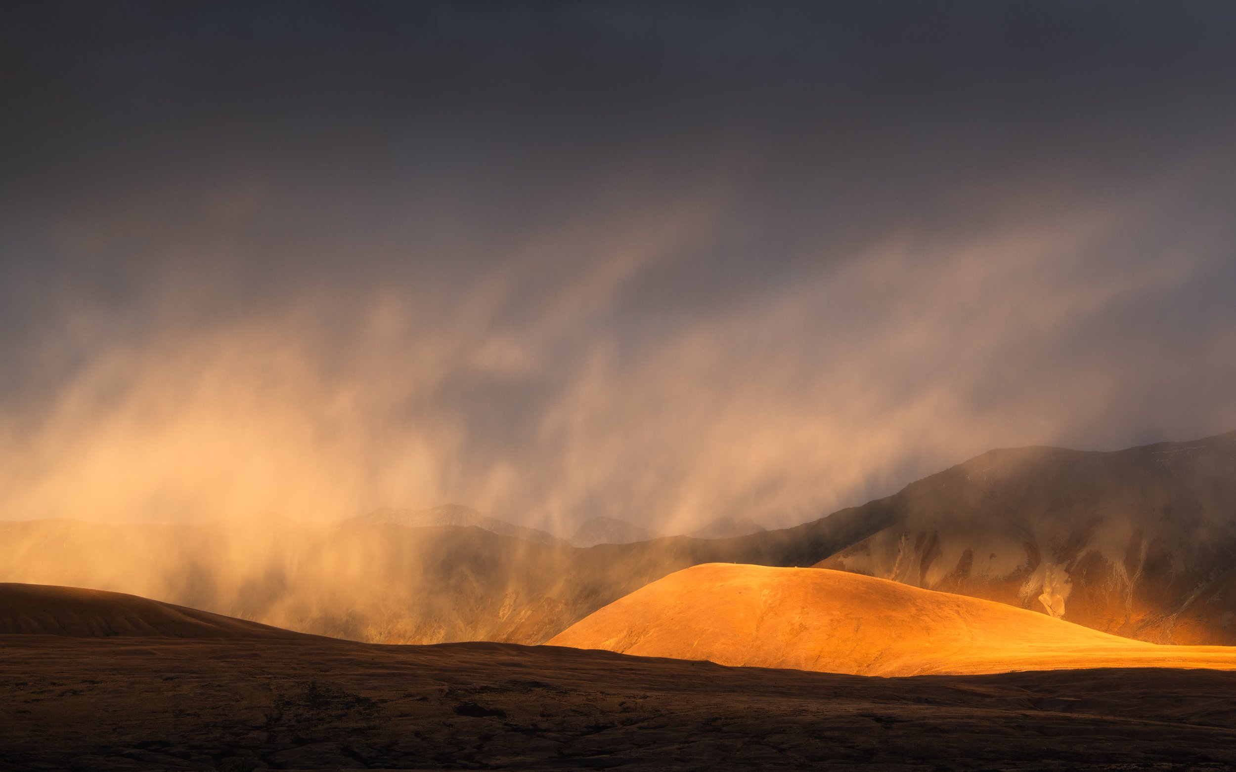 Samuele Quaranta - Landscape Photographer - Rain falling on sunset lit landscape with hills on background .jpg