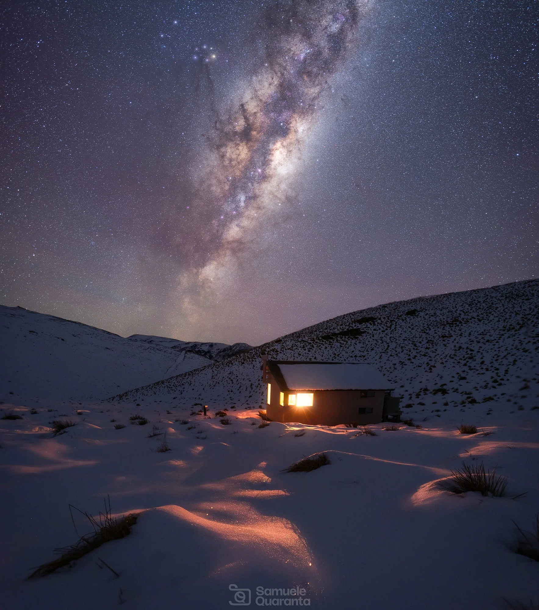 Milky Way over snowy landscape and lit up mountain hut in New Zealand - Samuele Quaranta 