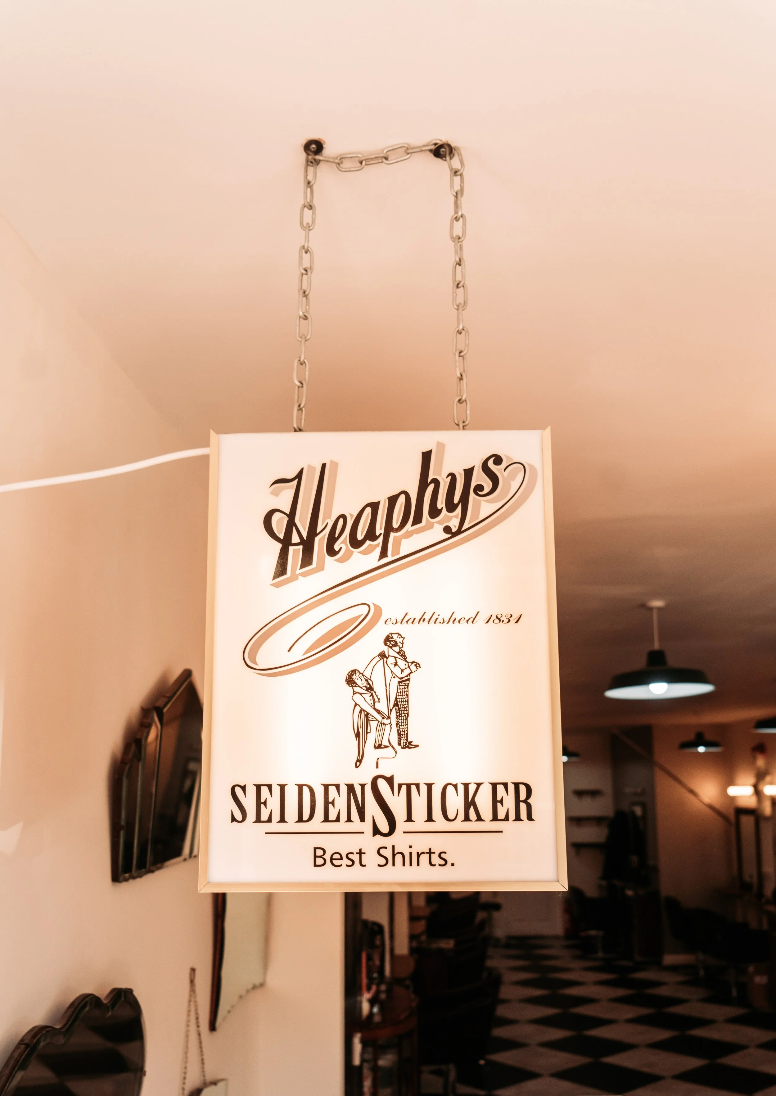 Happiness store sign hanging from ceiling chains, promoting shirts and stickers, with the establishment date 1834.