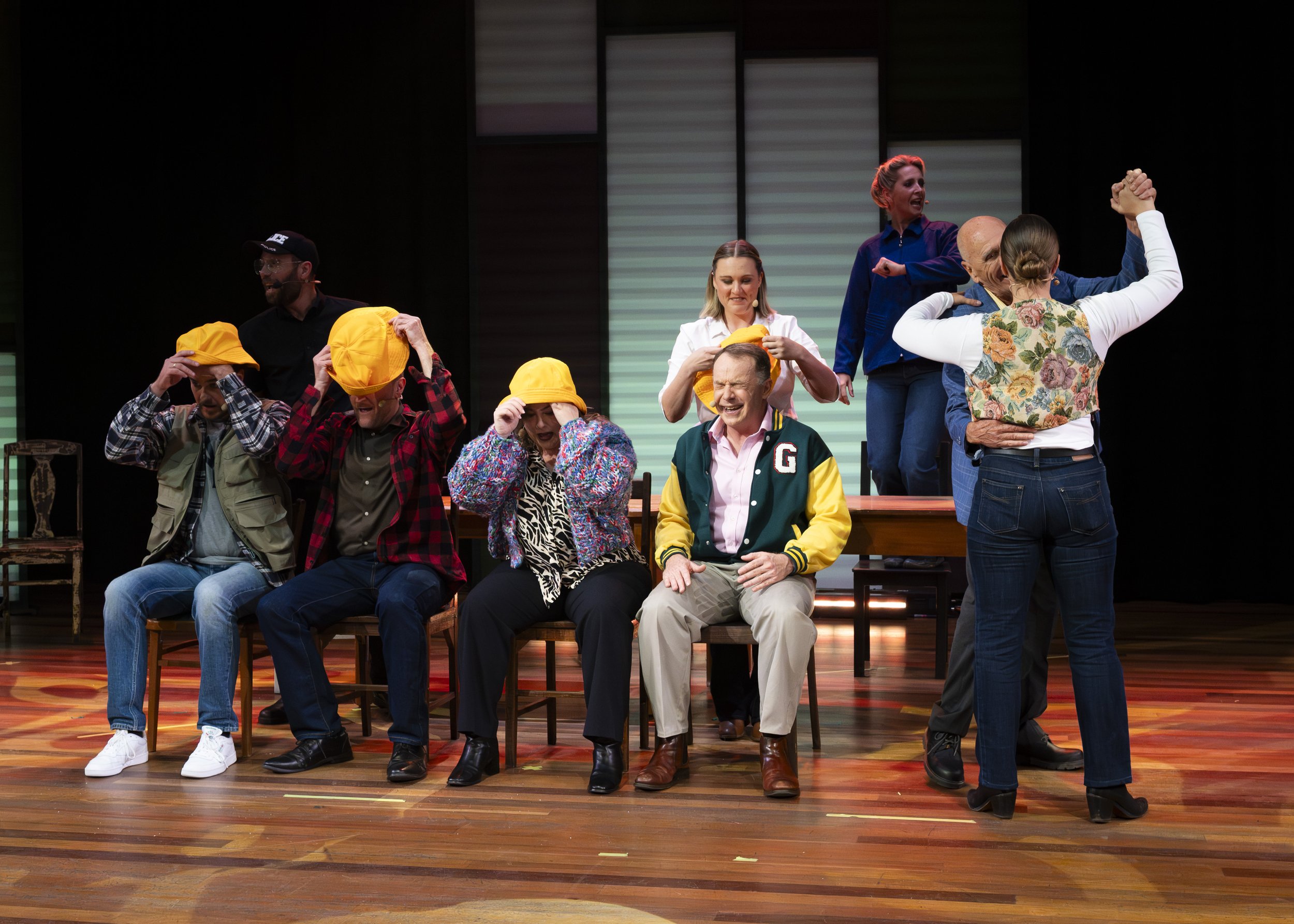 A group of people on stage participating in a theatrical performance, with some sitting and others standing or embracing.