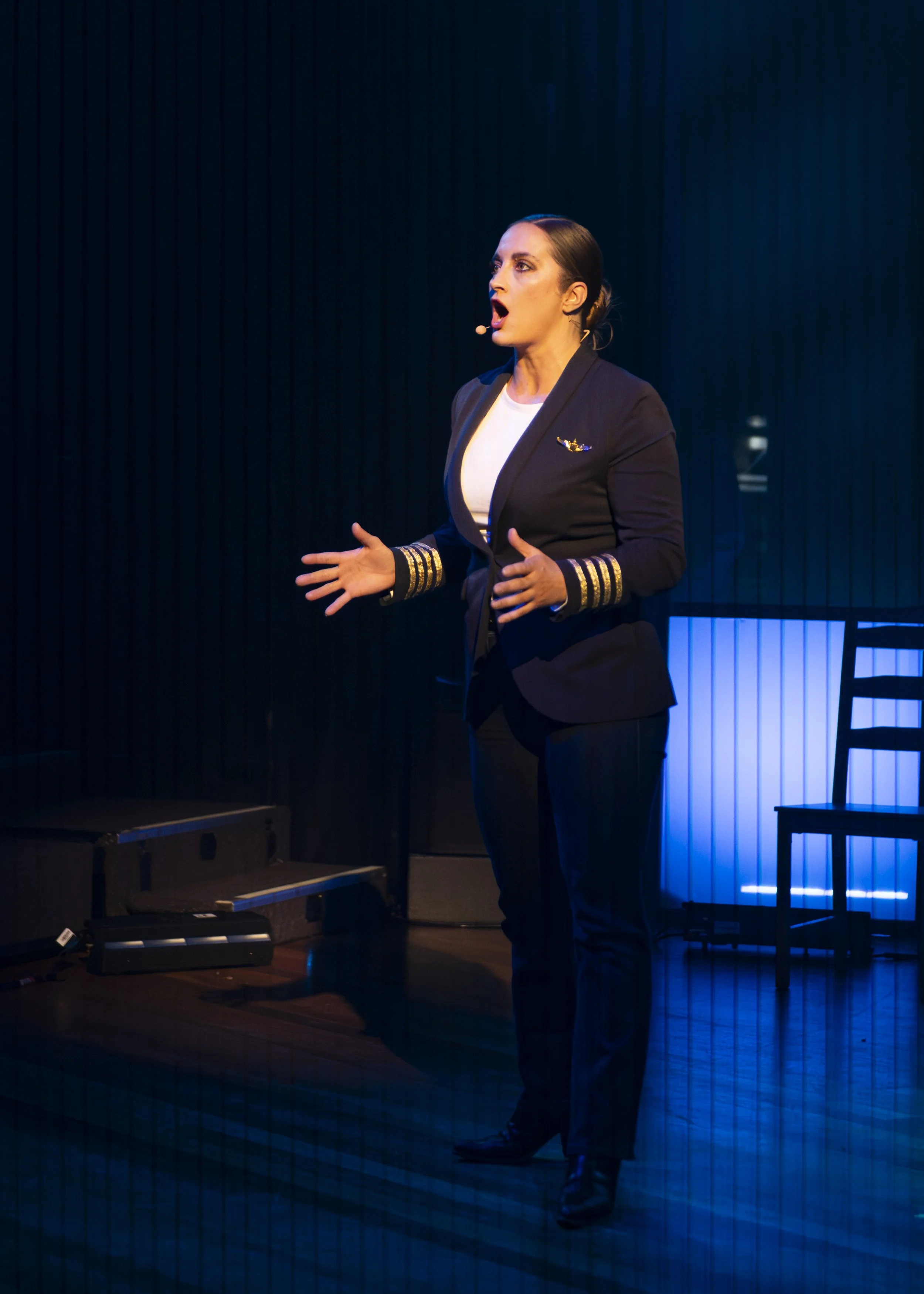 Woman in a pilot's uniform giving a speech on stage with a black curtain background.