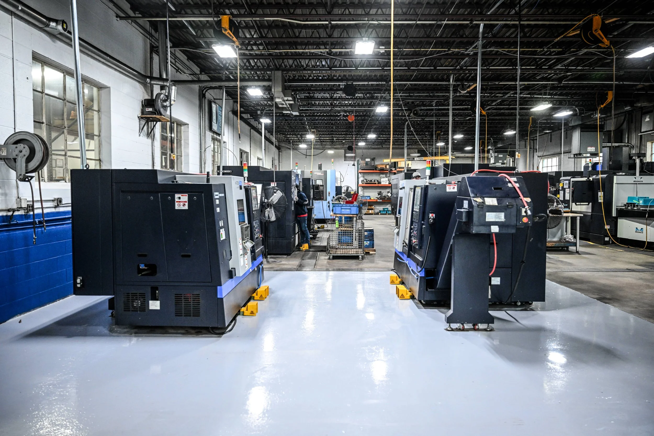 Rand Machine, Falconer, NY, Industrial manufacturing facility with multiple CNC machines and overhead cranes, large windows, and a glossy polished floor.