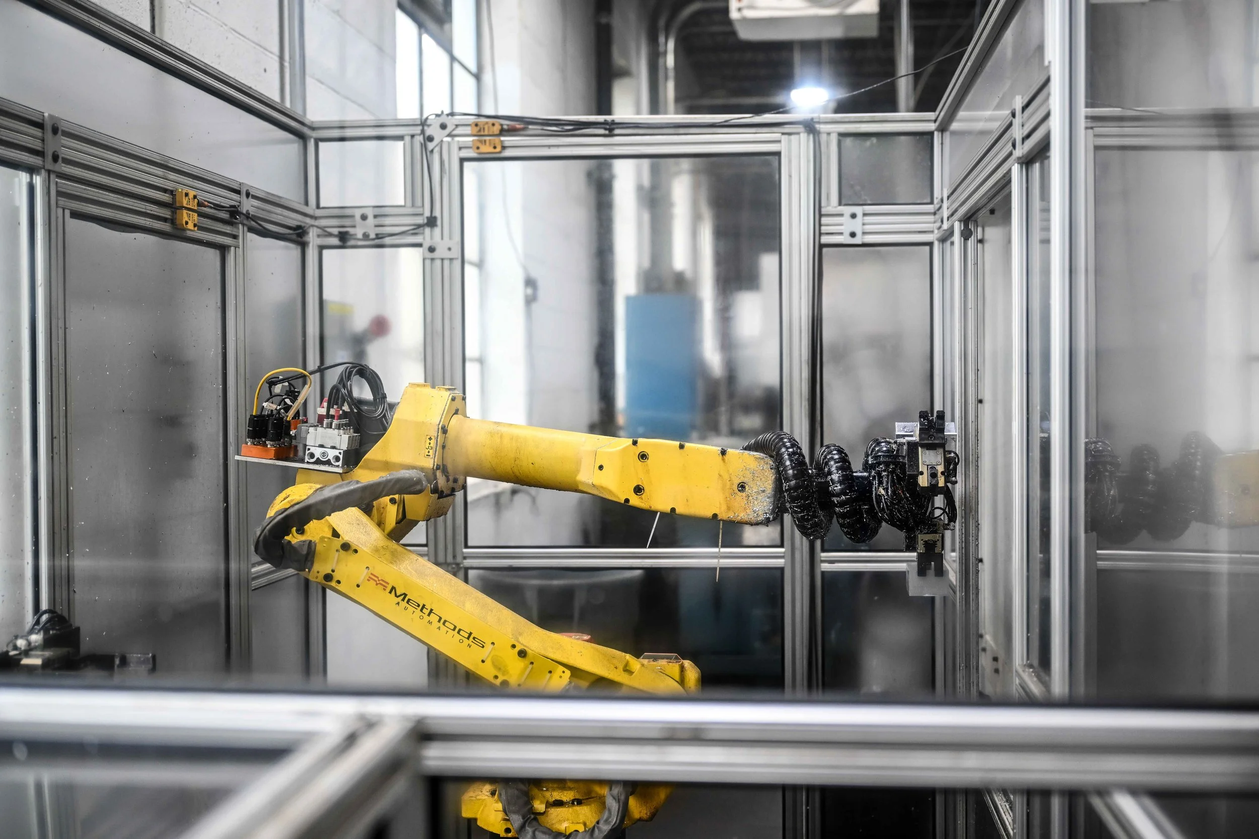 Industrial robotic arm inside a metal framework structure, with visible cables and electronic components, in a factory or workshop setting.