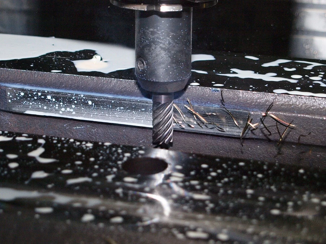 Close-up of a drill bit cutting into metal on a milling machine, with metal shavings and lubricant.