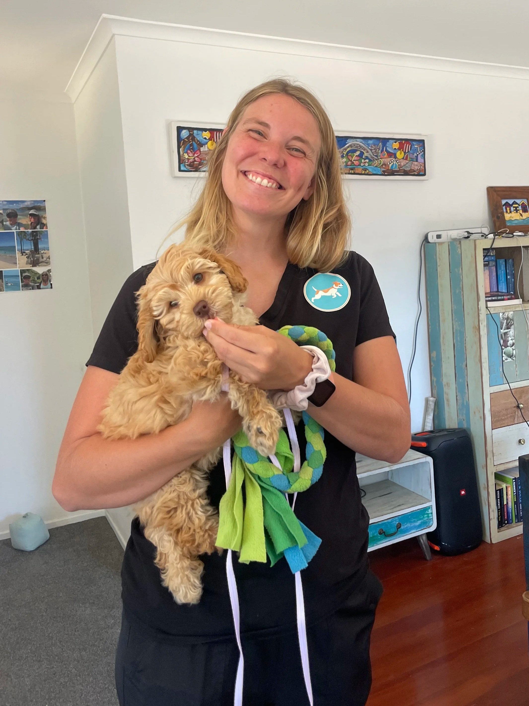 A smiling woman holding a fluffy, light brown puppy inside a house.