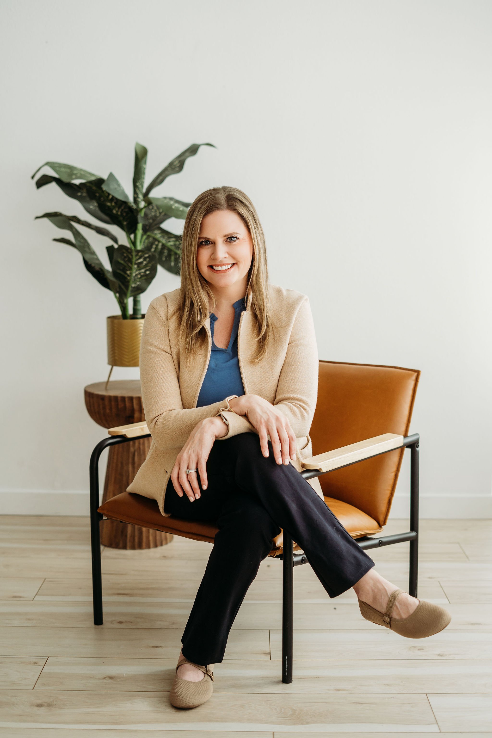 A woman sitting on a chair with a potted plant behind her, smiling at the camera.