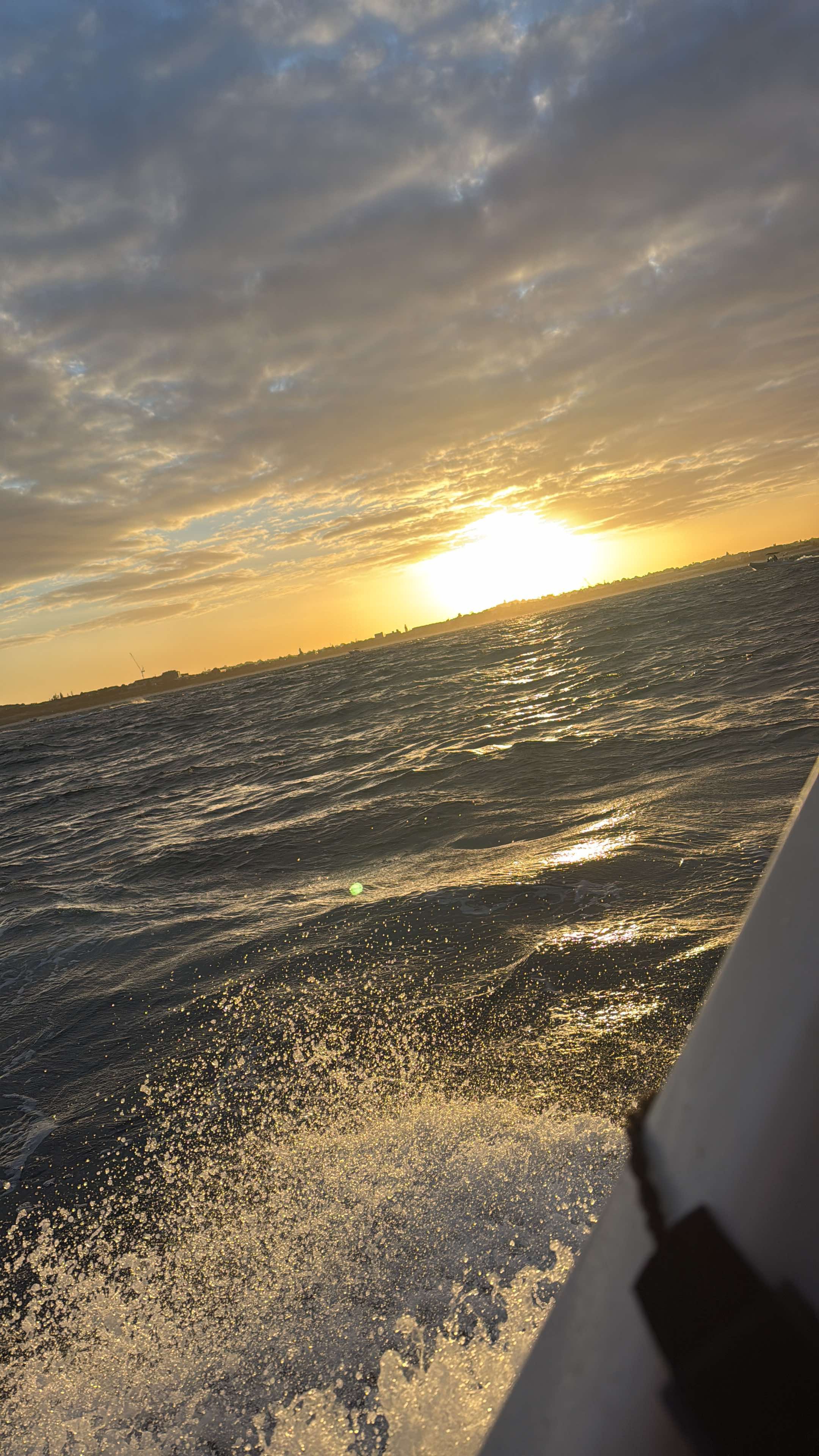 Orange sunset taken from the side of the support boat, the wash from the bow visible in the bottom of the shot