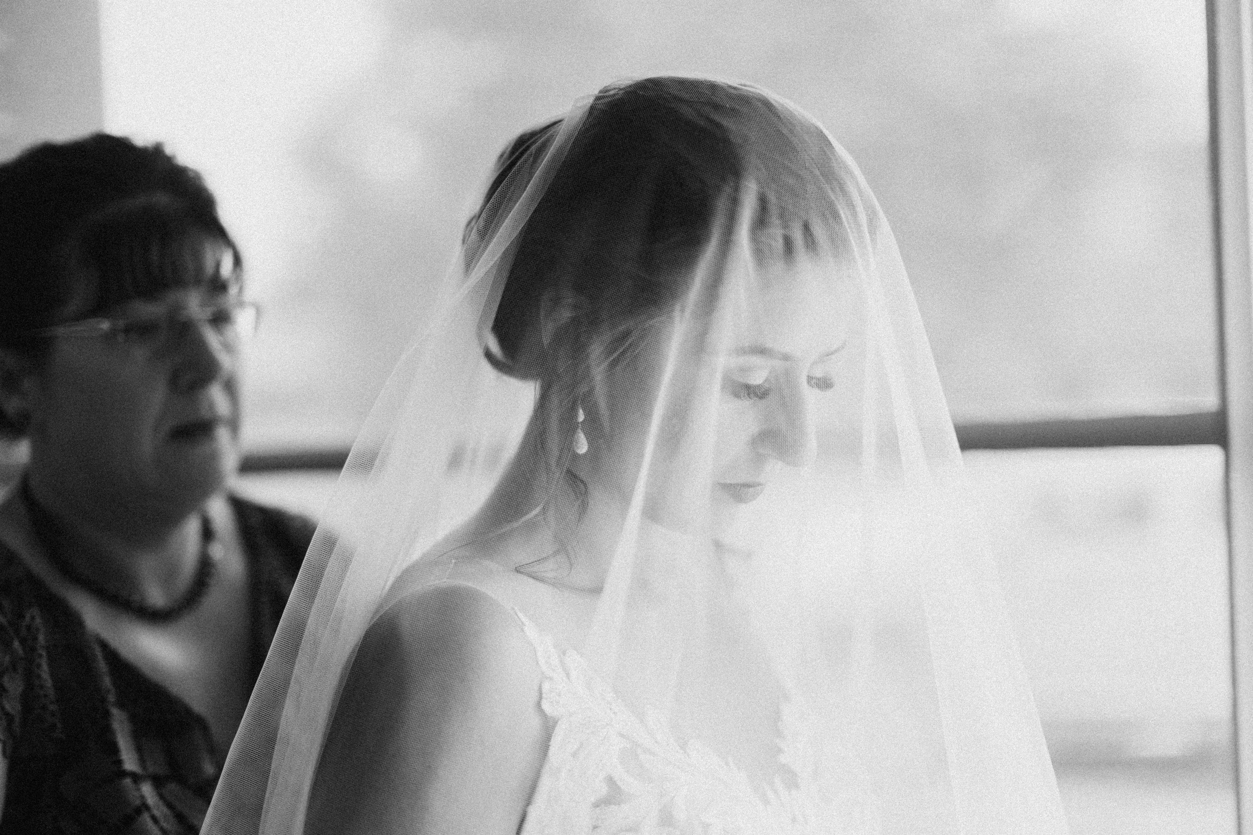 Bride wearing a veil, black and white photo, woman in background.