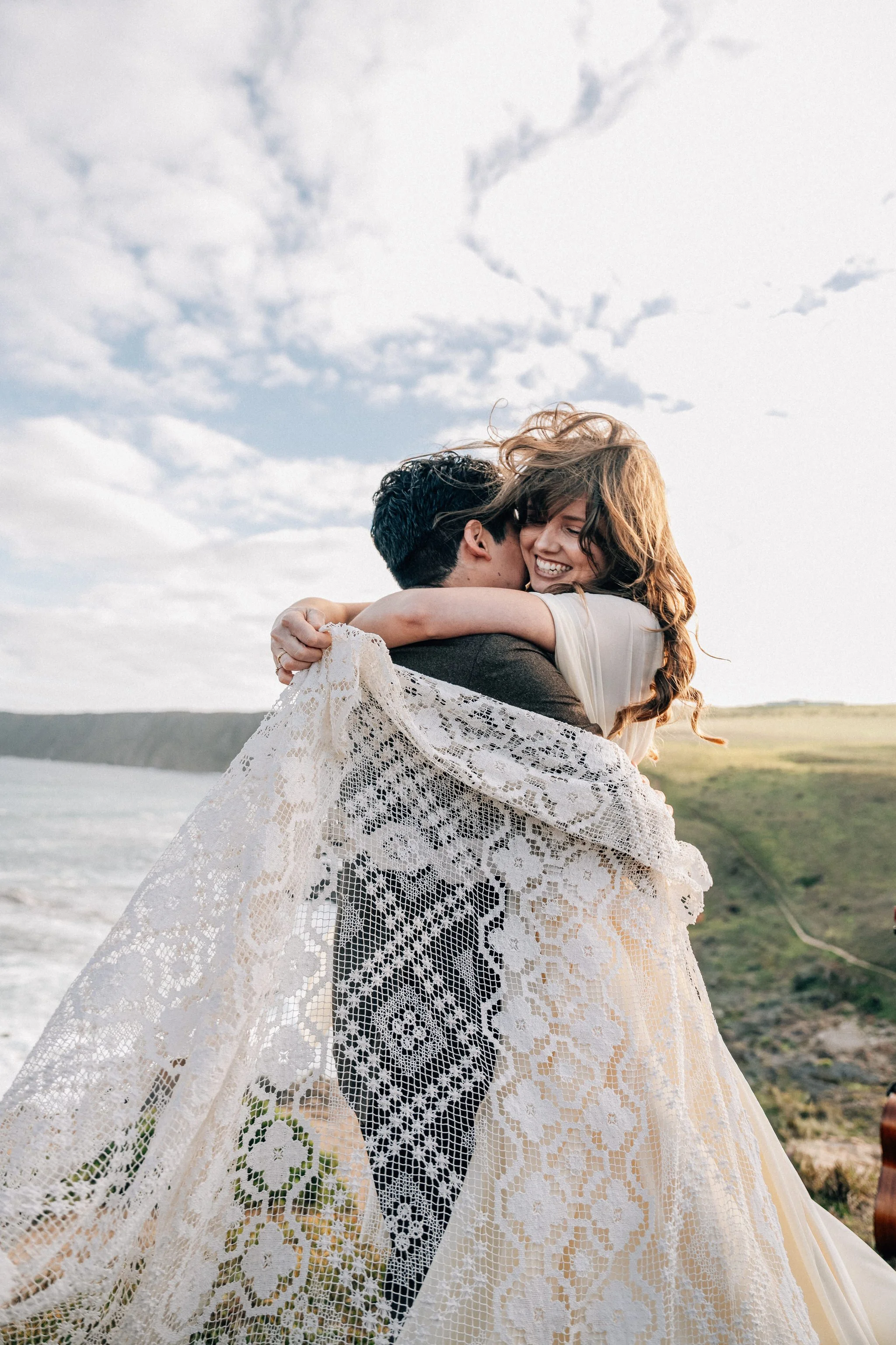 Young wedding couple embracing at the top of a cliff under the sky.