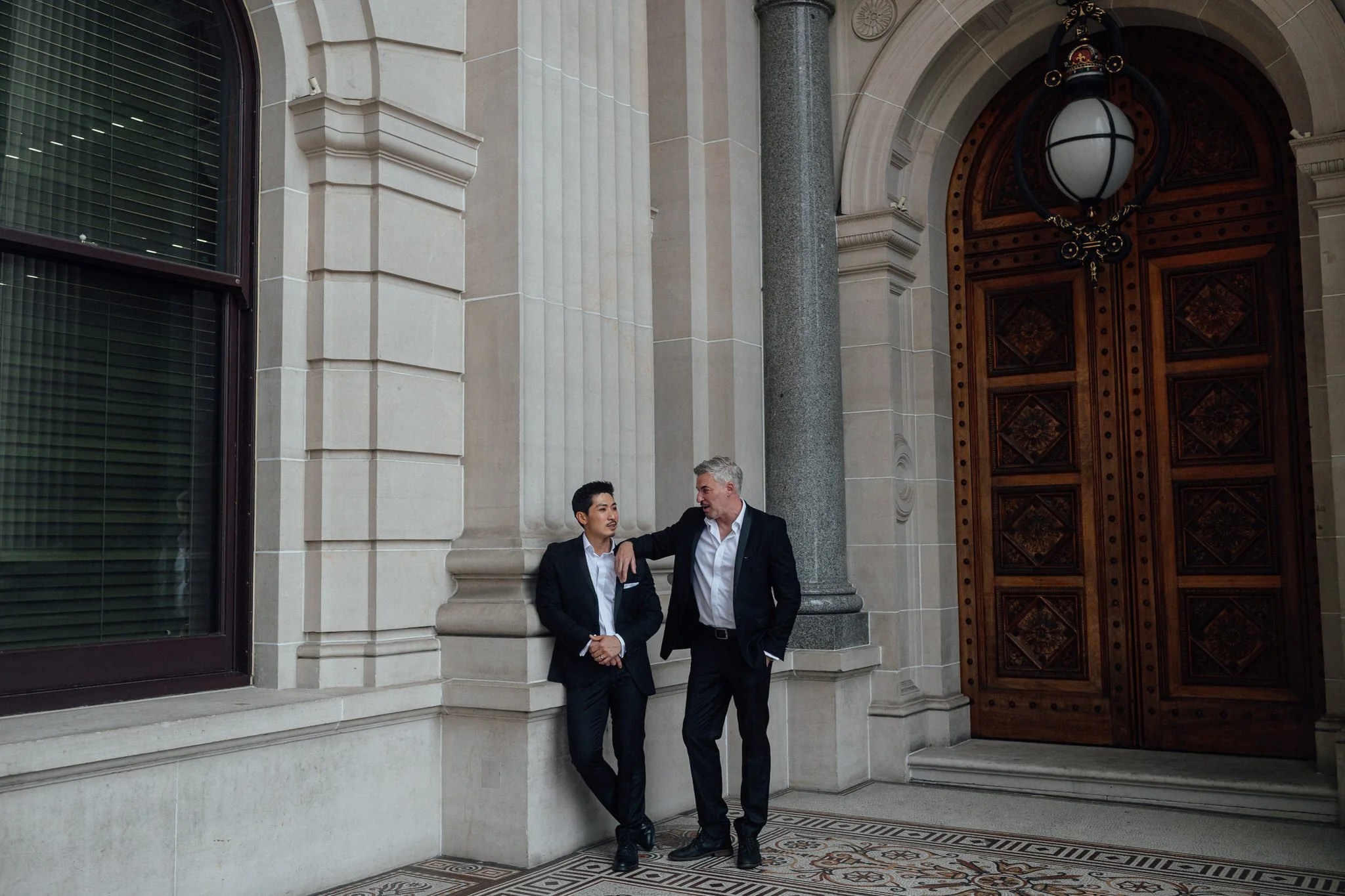 one groom leaning on the other groom's shoulder at the top of parliament house