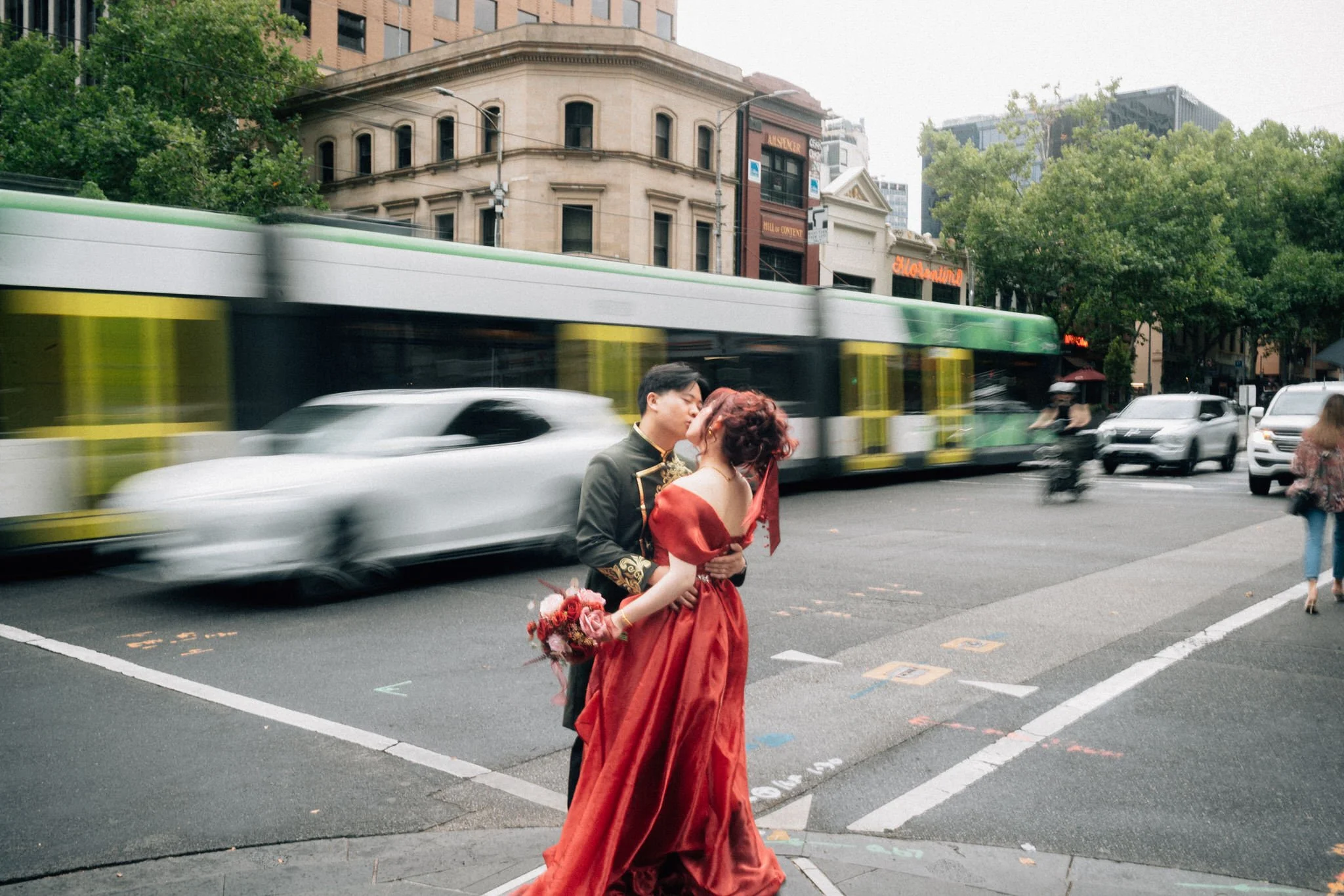 Couple kissing with a tram moving past them on the side of a street