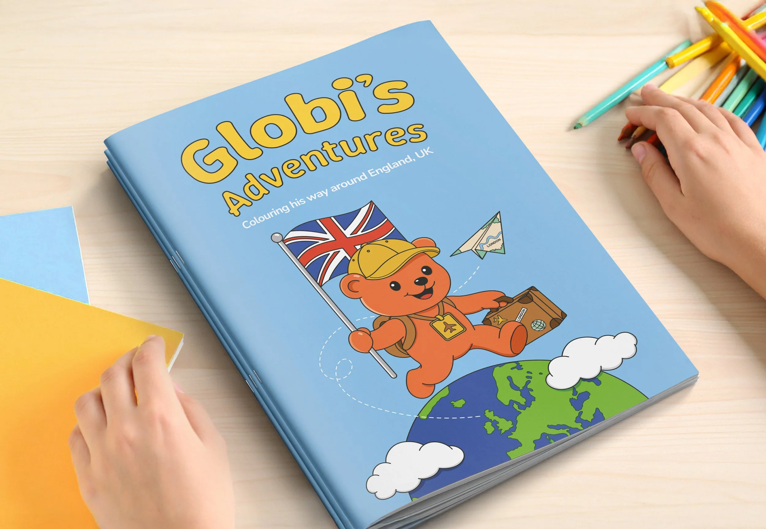Children's coloring book titled 'Globi's Adventures: Colouring his way around England, UK' with a cartoon bear holding a Union Jack flag and a suitcase, flying over the globe with clouds and a paper plane nearby.