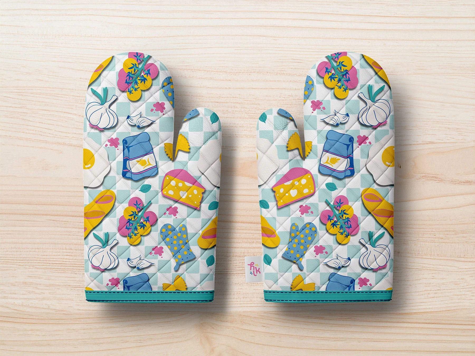 A pair of oven mitts with a colorful pattern of vegetables, cheese, and kitchen items on a light wooden surface.