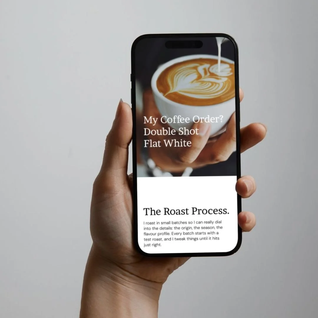 A person holding a smartphone displaying a coffee shop menu with a picture of a latte and text about coffee orders and the roasting process.