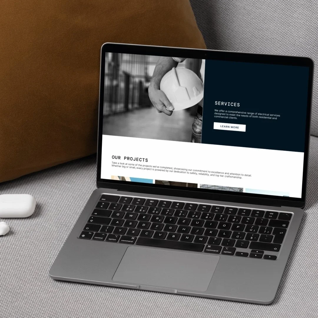 A laptop on a desk displays a website showcasing electrical services and projects, with a black and white image of a person holding an electrical component in the background.