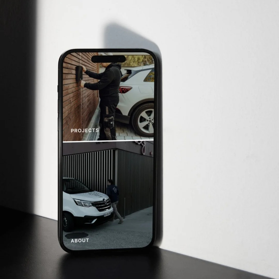 Smartphone displaying a website with two images, one of a person installing a security camera on a wooden wall and another of a person near a white van, with the words "PROJECTS" and "ABOUT" visible.