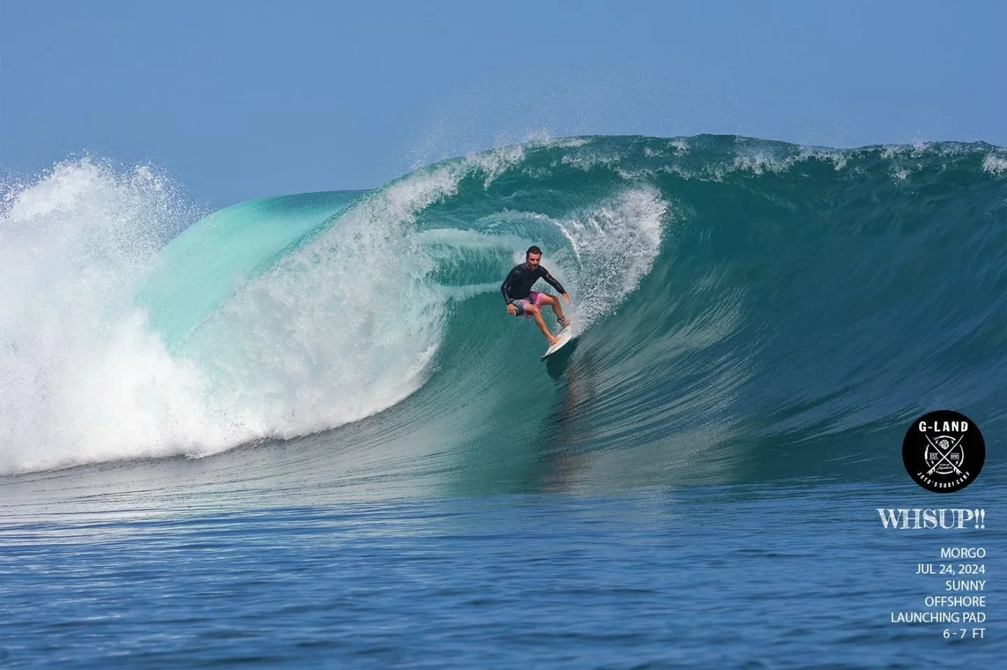 Surfer riding a large wave at G-Land, with clear blue skies and ocean.