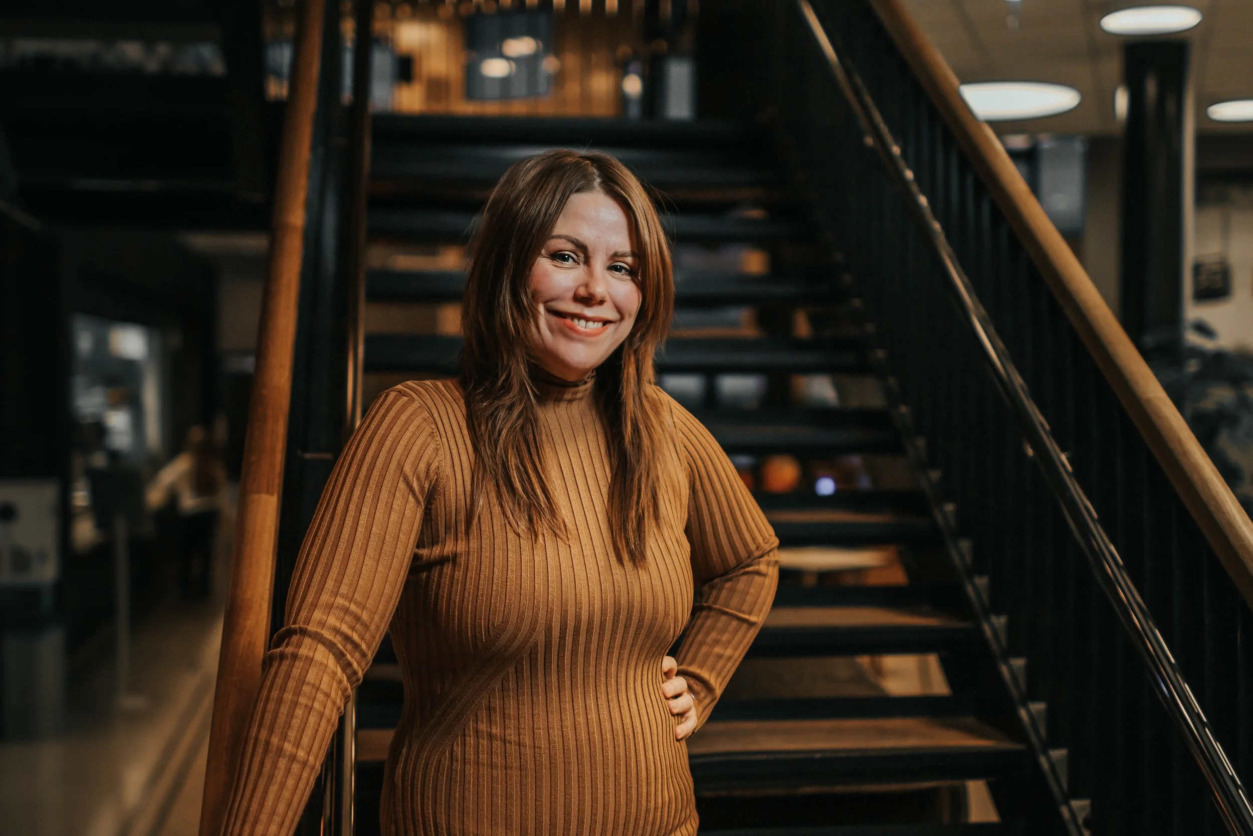 Kvinne smilende foran en trapp i en innendørs restaurant eller kafé.