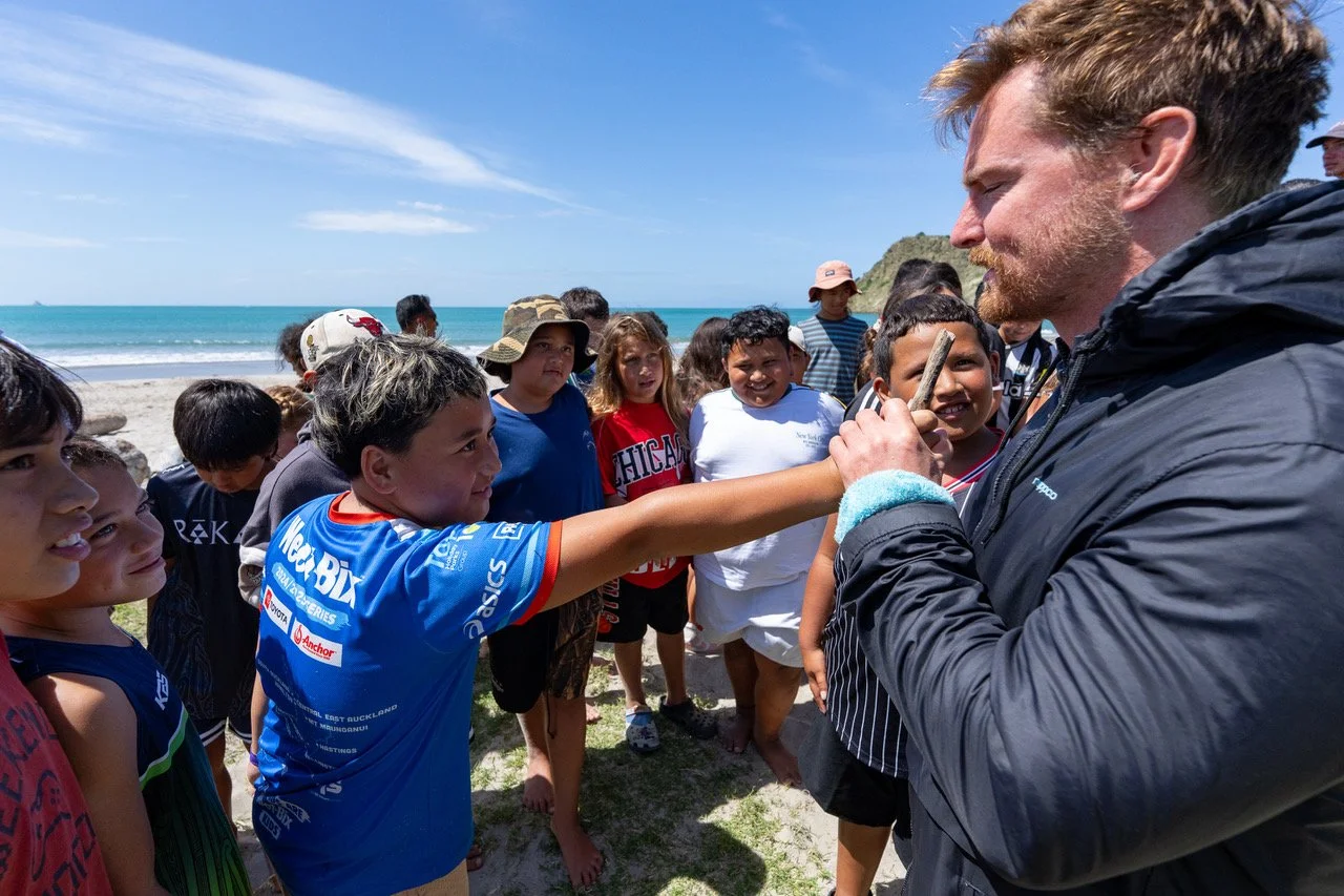 Swim4TheOcean: Jono Ridler greets tamariki from a local kura at Whāngārā Beach, photographed by Joshua McCormack, 2026