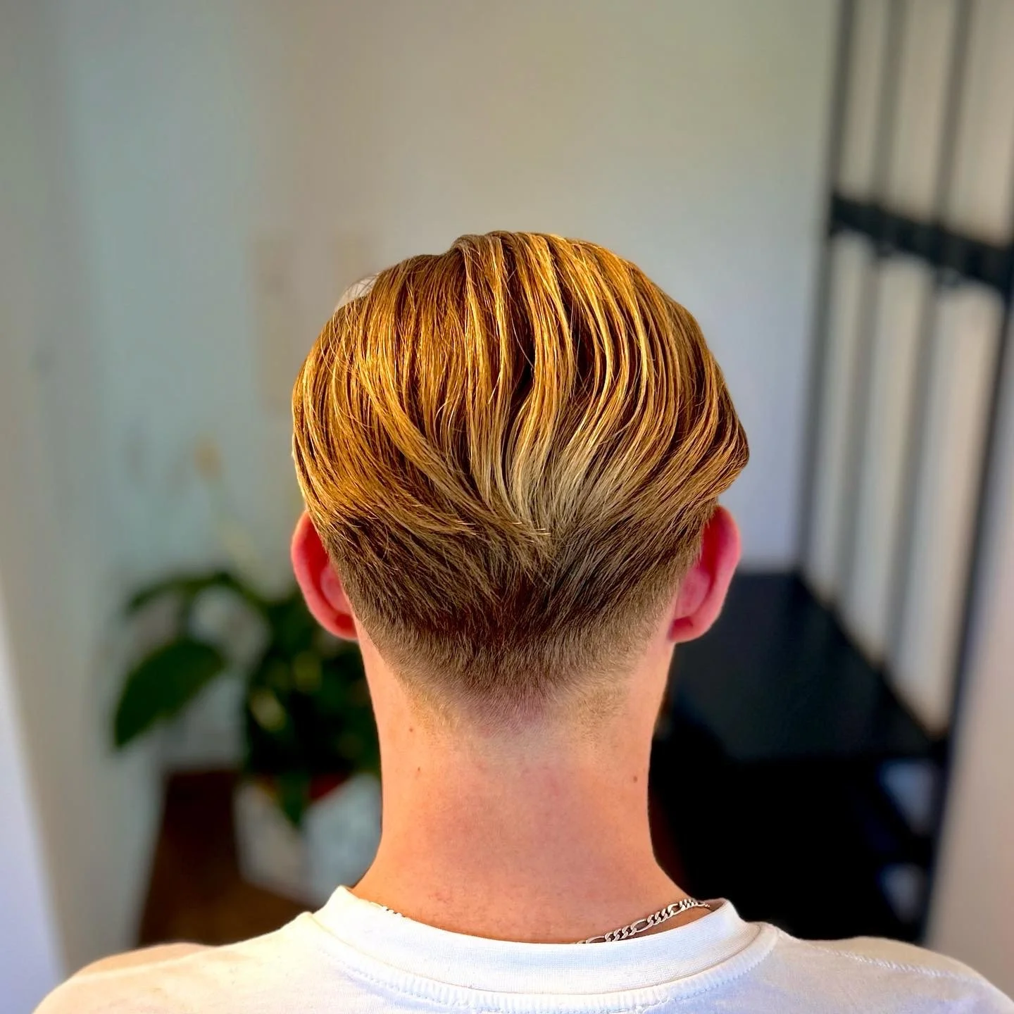 Hinterkopf einer Person mit blondem Haar, das sorgfältig gestylt ist, im Innenbereich aufgenommen.
