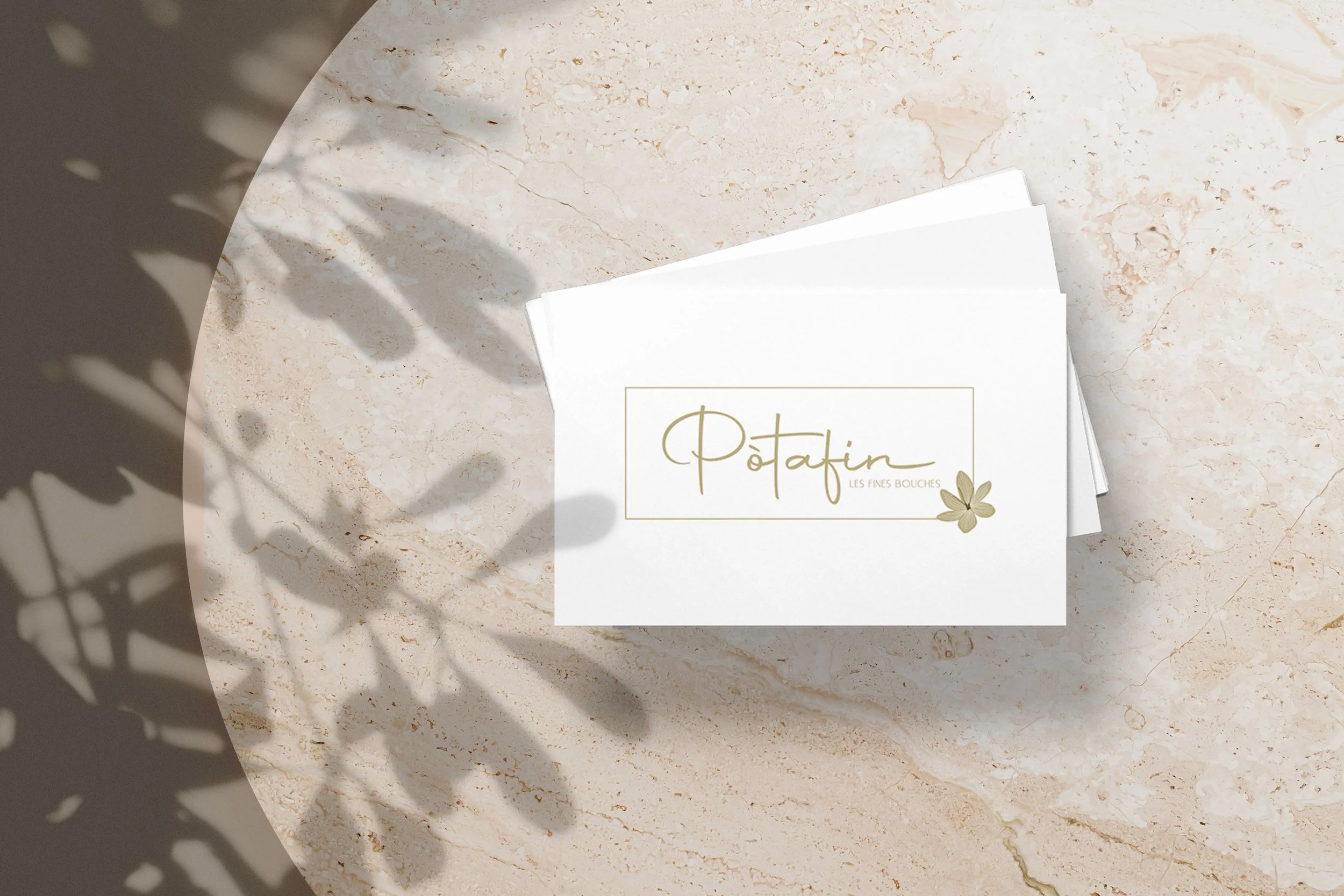 Cartes blanches avec le logo et le nom Potatin, posées sur une surface en marbre beige avec une ombre de feuilles portée par la lumière