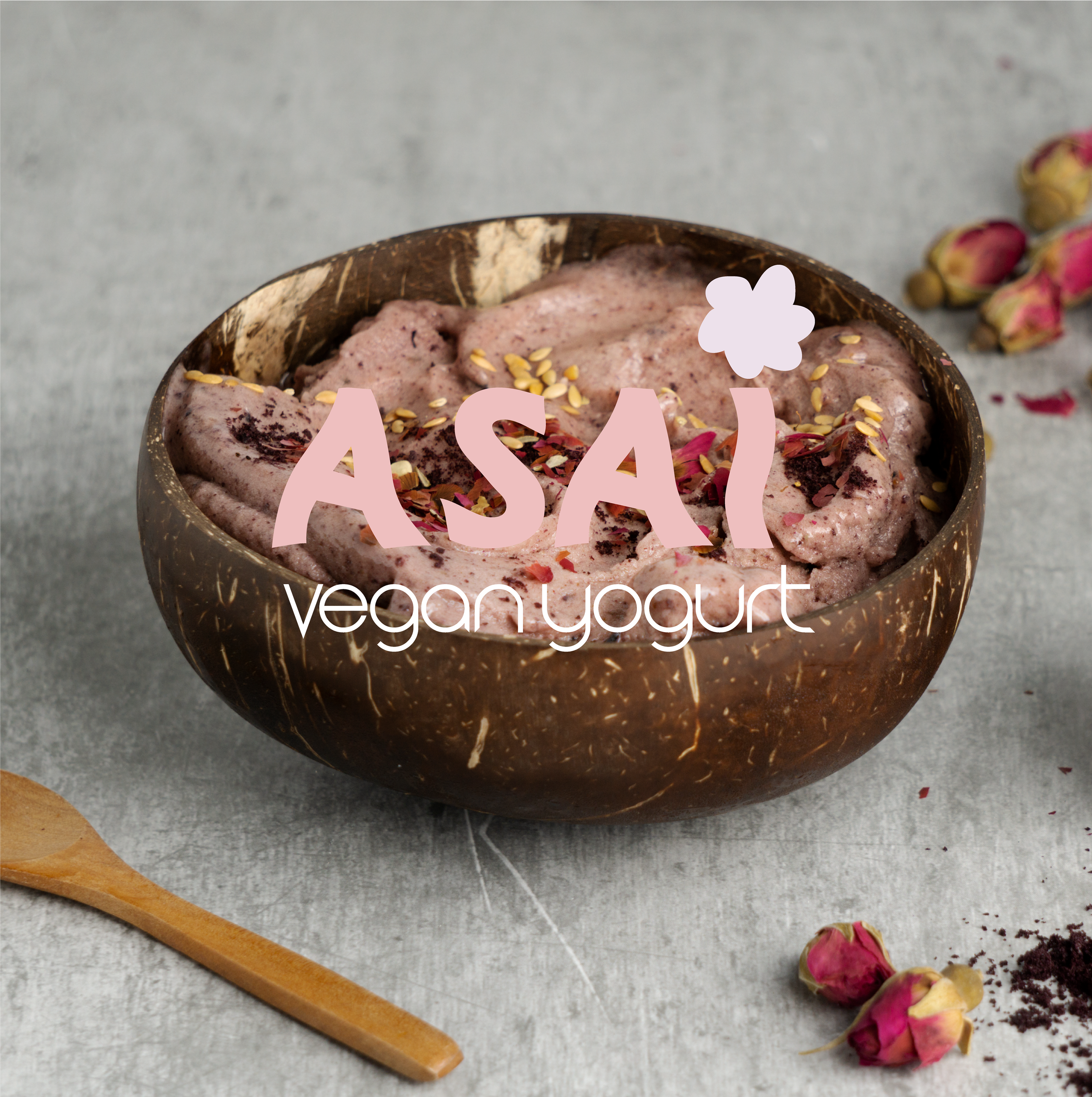 Bol en forme de noix de coco contenant un yaourt végétalien à la fraise, garniture de graines et de morceaux de fruits, avec des fleurs de rose séchée autour.