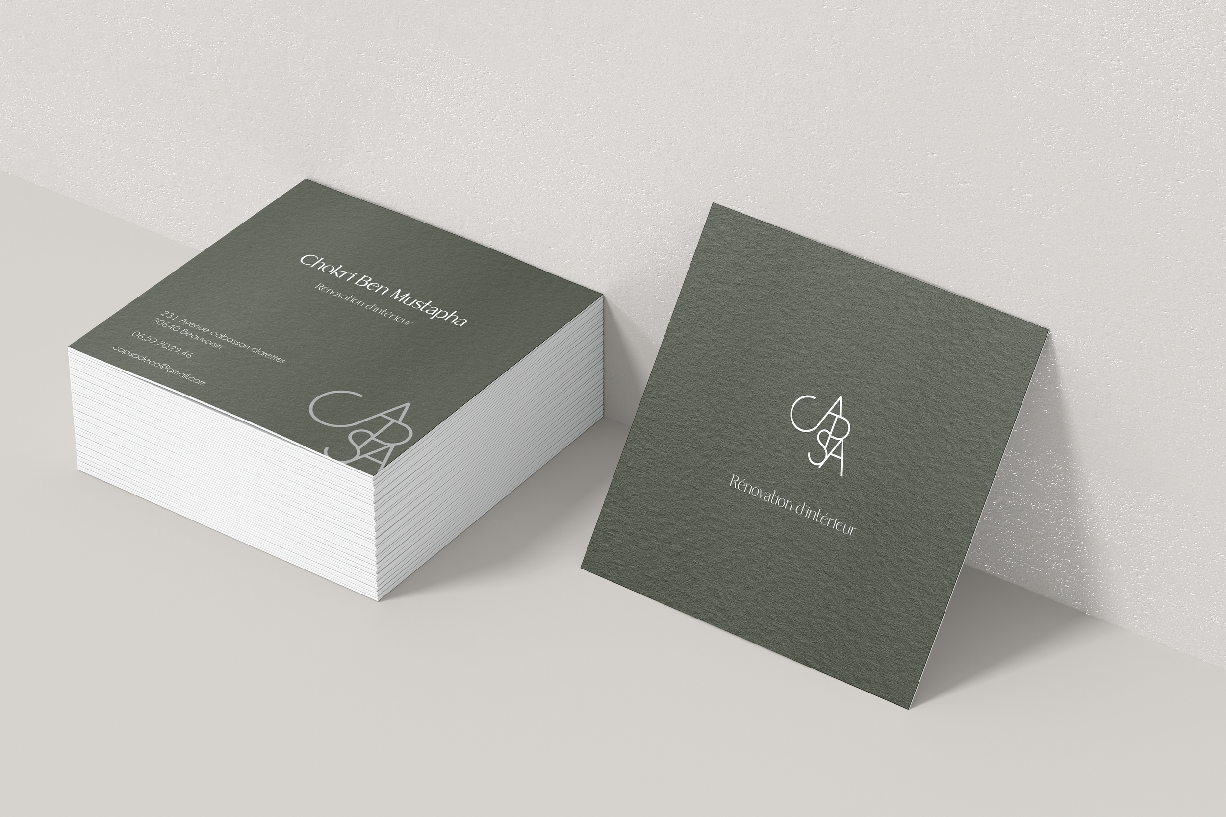 Paquet de cartes de visite pour Chokri Ben Mustapha et une carte de visite affichée à côté, avec un fond gris foncé et un logo blanc, pour une rénovation intérieure.
