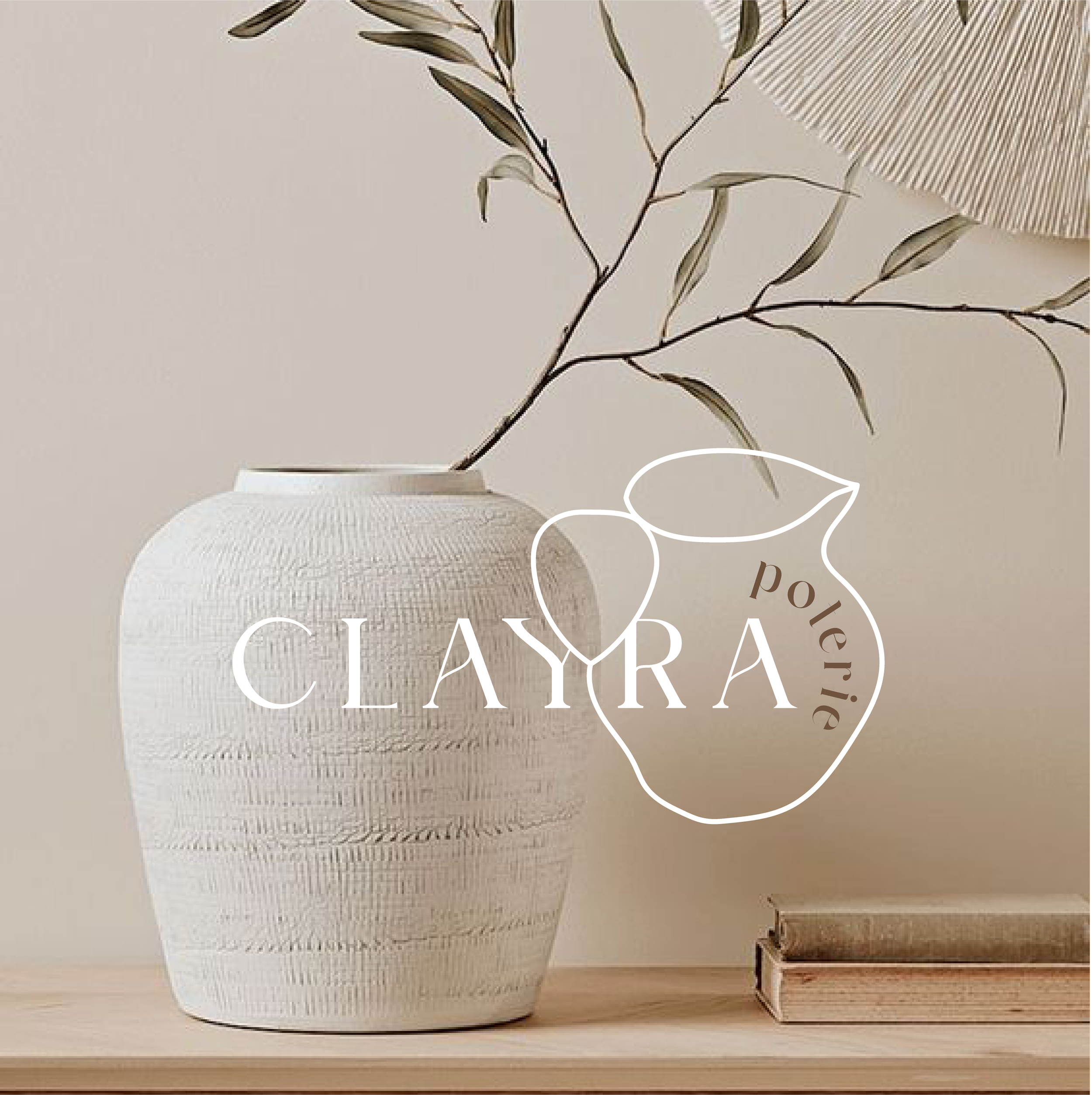 Une vaisse en céramique blanche avec des détails texturés, contenant une branche d'arbuste aux feuilles longues et fines, avec un livre posé à côté. Sur la photo, le texte "Claira" et "Polerie" est inscrit dans un design de fruit stylisé.