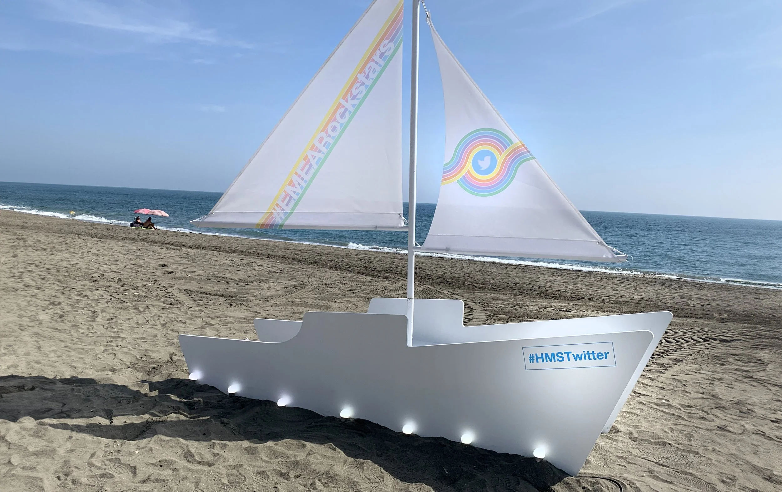 Event production of a white boat-shaped structure with logos installed at candado beach malaga. Photo oportunity decoration Málaga.
