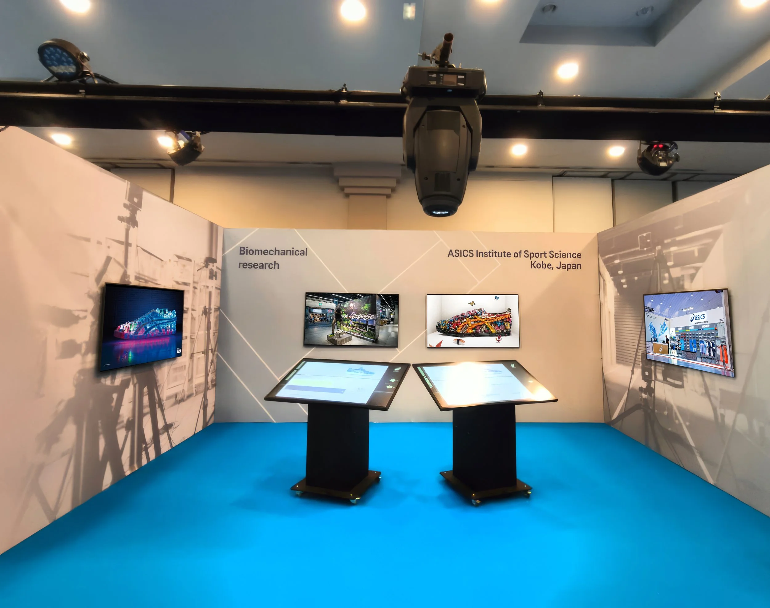Exhibition booth installation with three wall-mounted screens and two interactive display tables at ASICS corporate event in marbella spain.
