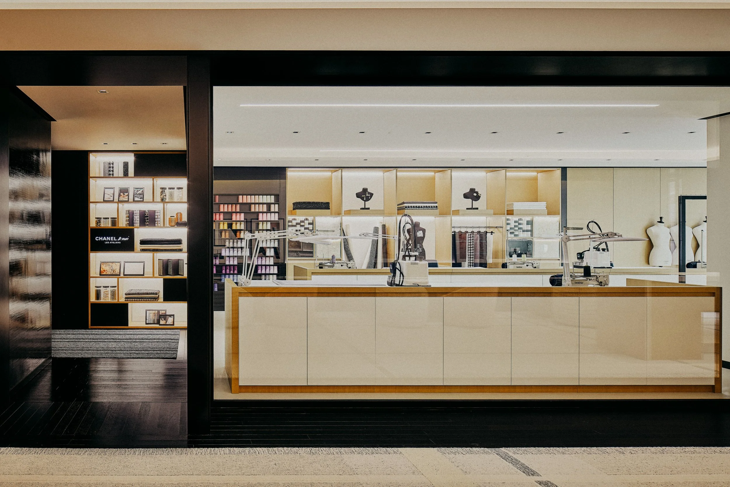 Interior of a modern store with shelves of fabric, mannequin busts, and sewing machines on a white counter.
