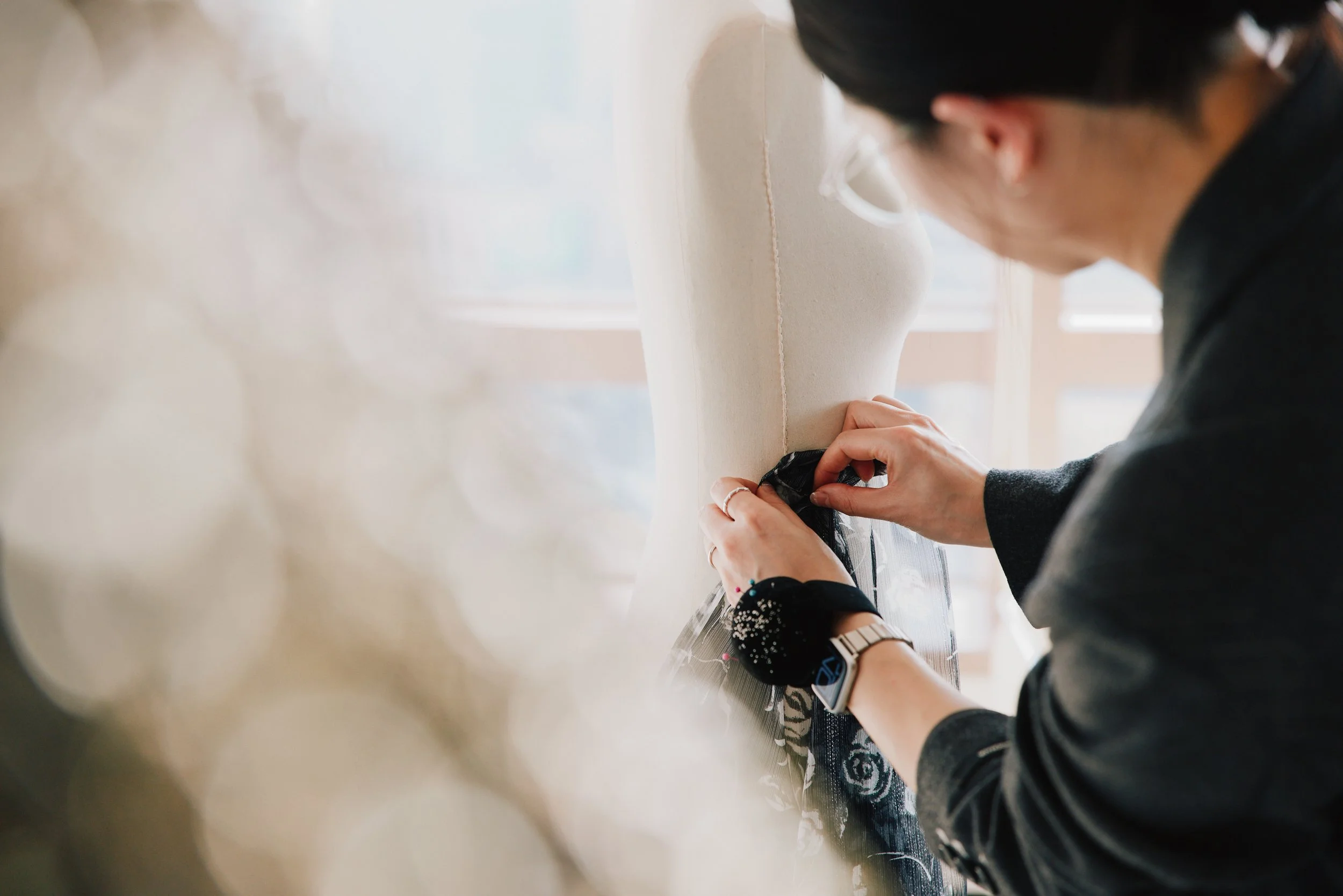 A person crafting or sewing fabric on a table, with focus on their hands and materials, in a well-lit workspace.