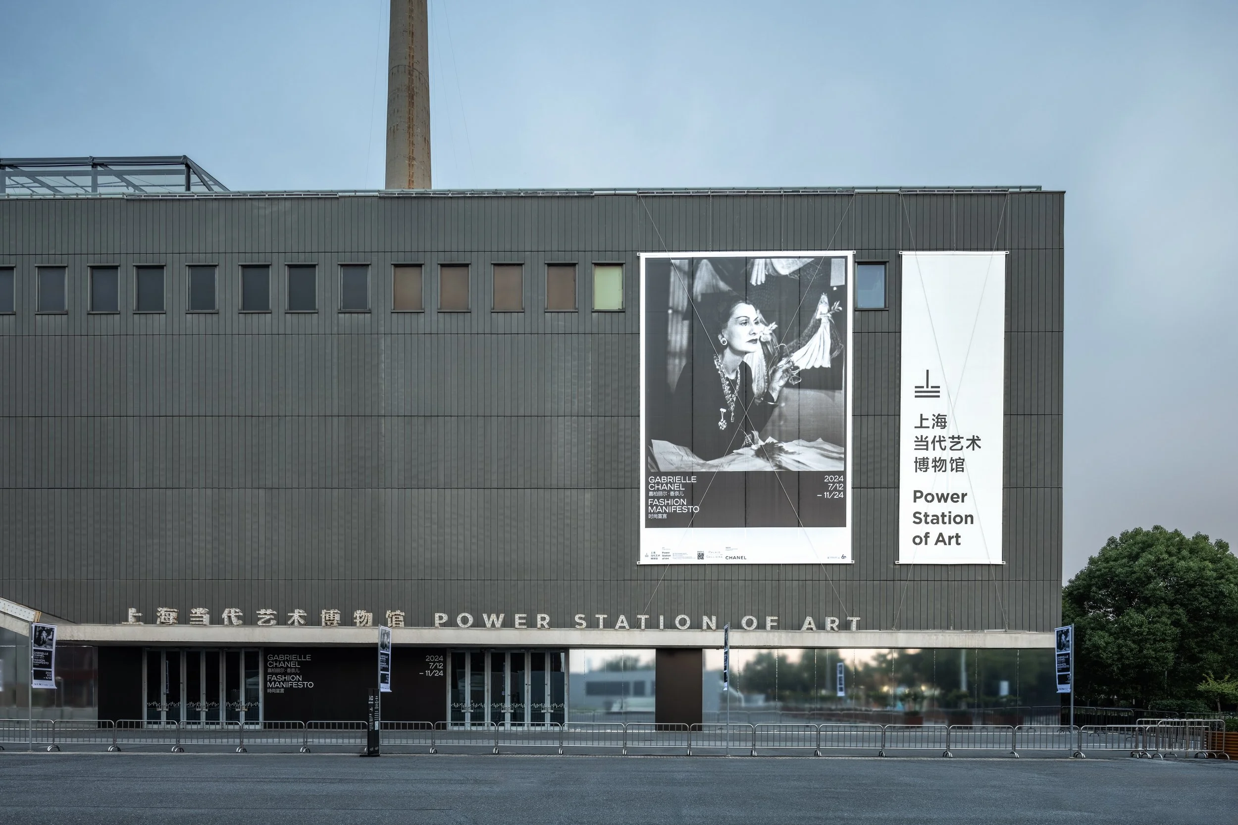 Exterior of the Power Station of Art museum with large vertical banners, one showcasing a black and white portrait of a woman and the other with the museum's name in Chinese and English.
