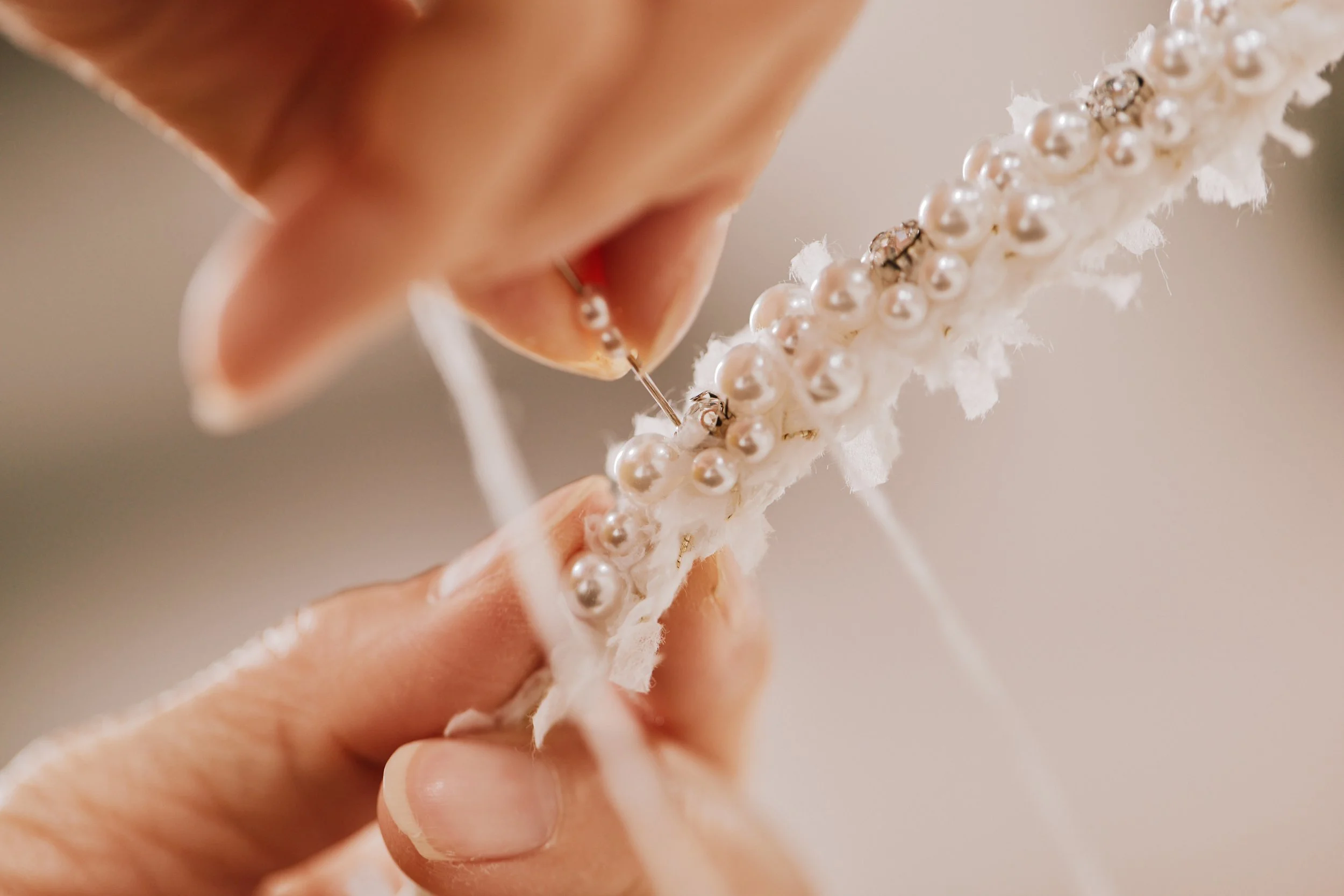 Close-up of a person’s hand holding a decorative item embroidered with pearls and rhinestones, with part of the person's face visible in the background.